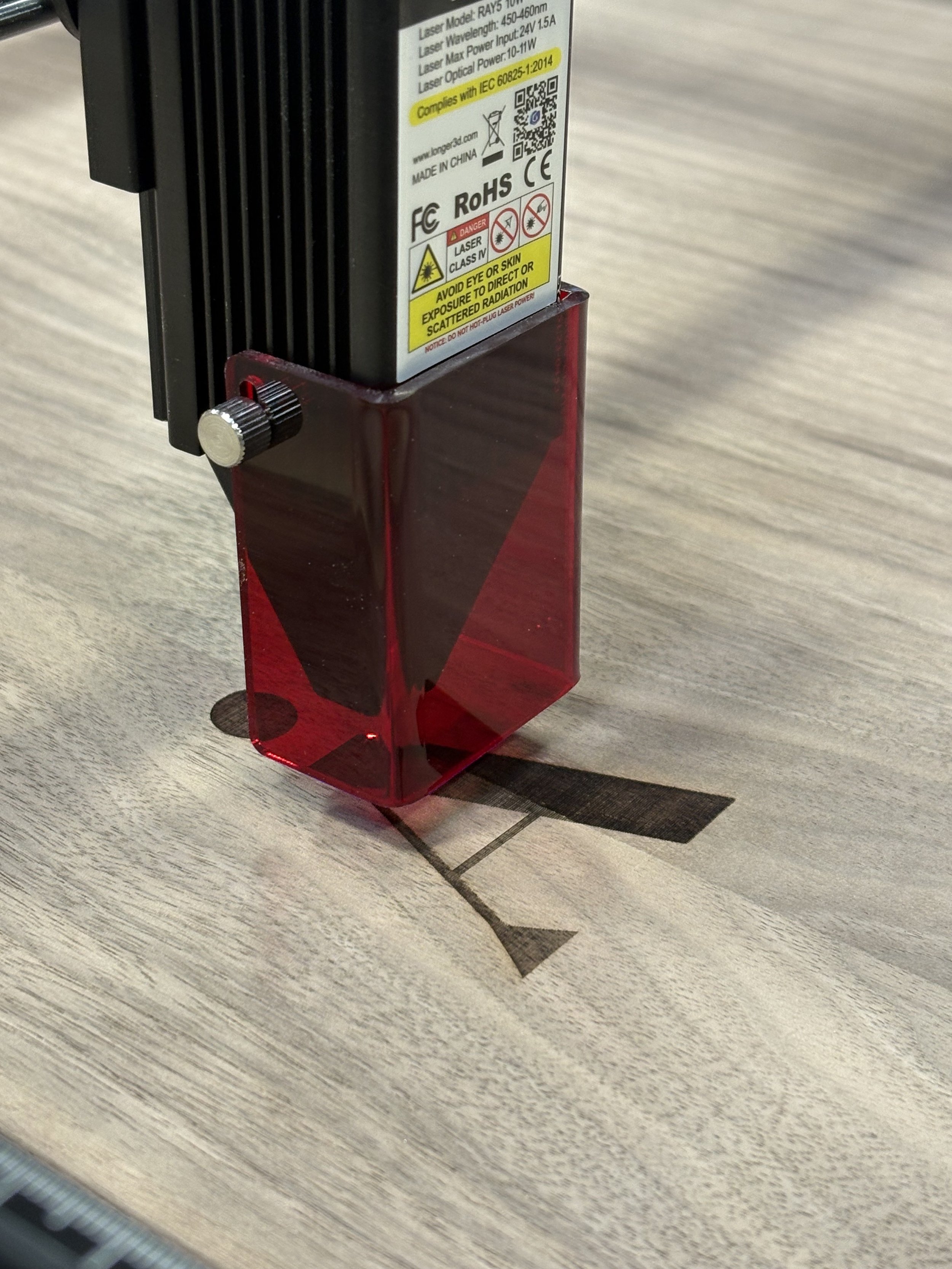Close-up of a laser device with warning labels and a red protective cover, placed on a wooden surface.