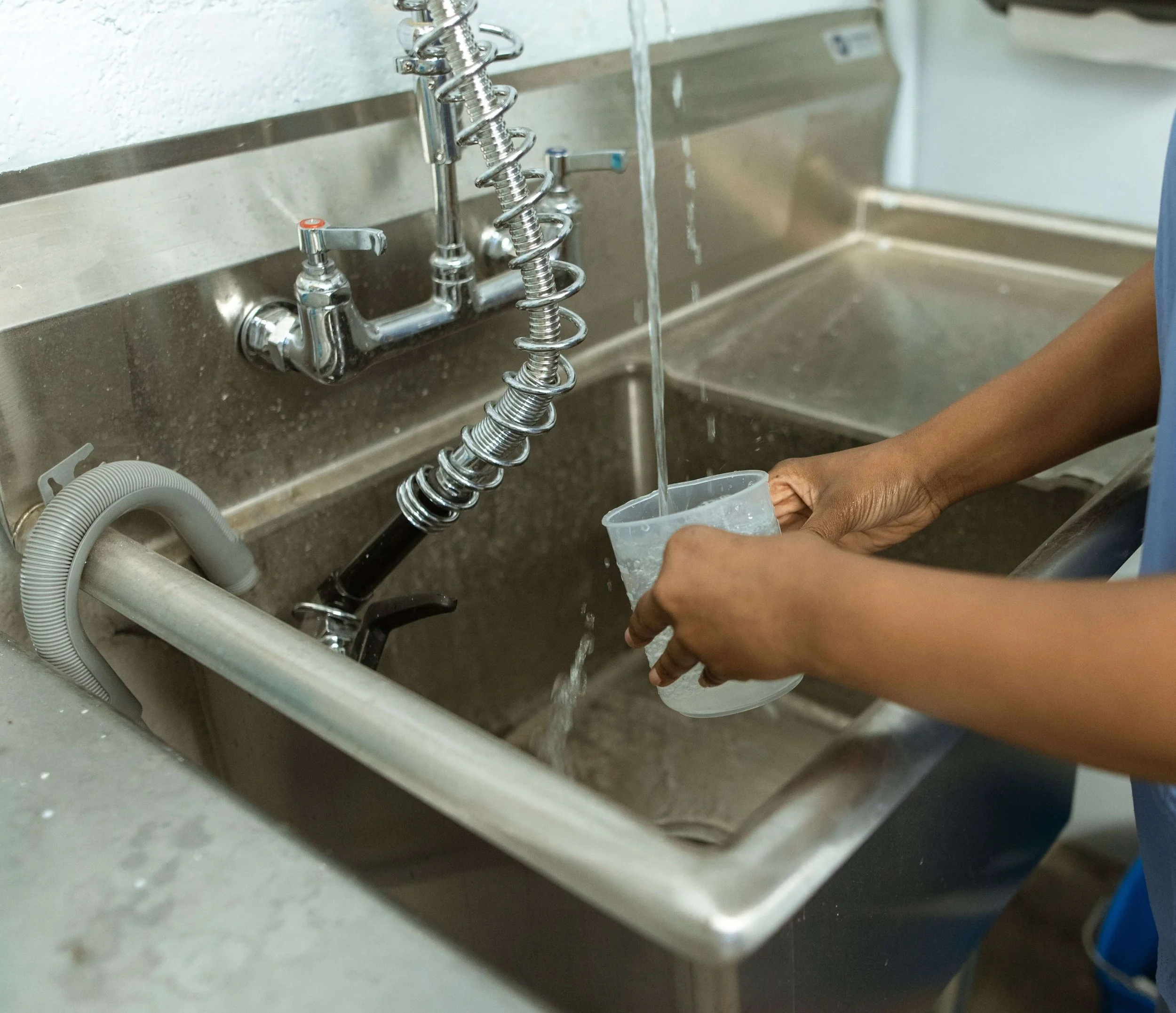 A stainless steel restaurant commercial sink with a worker filling up a cup of water.
