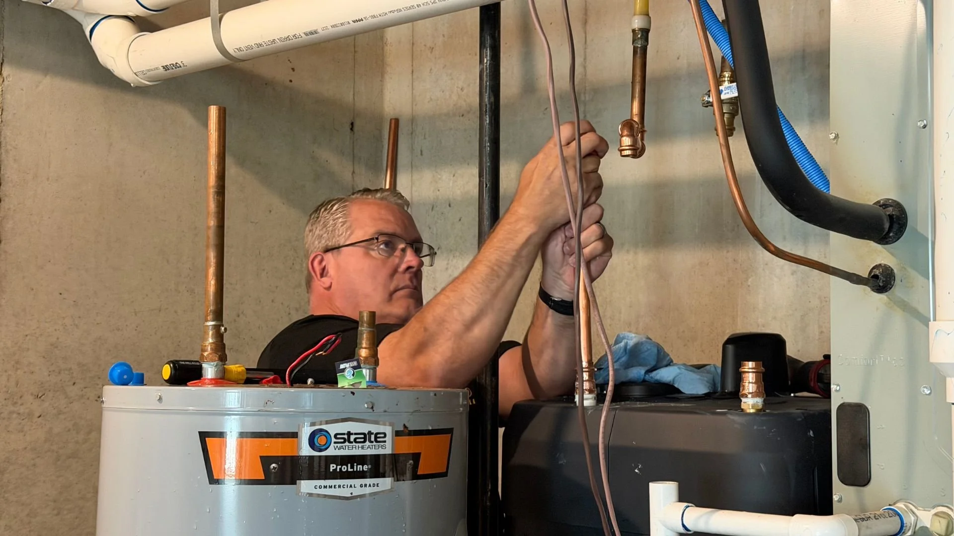 Bristol Plumbing's Mike Covington working on plumbing by concrete basement wall with copper pipes and fittings.