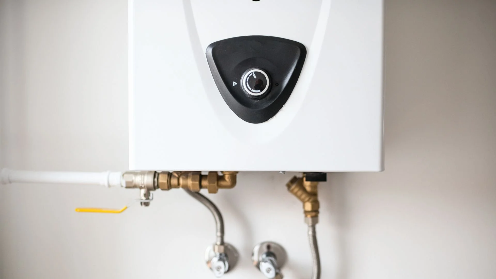 A white wall-mounted tankless water heating system with a black control dial and brass pipes.