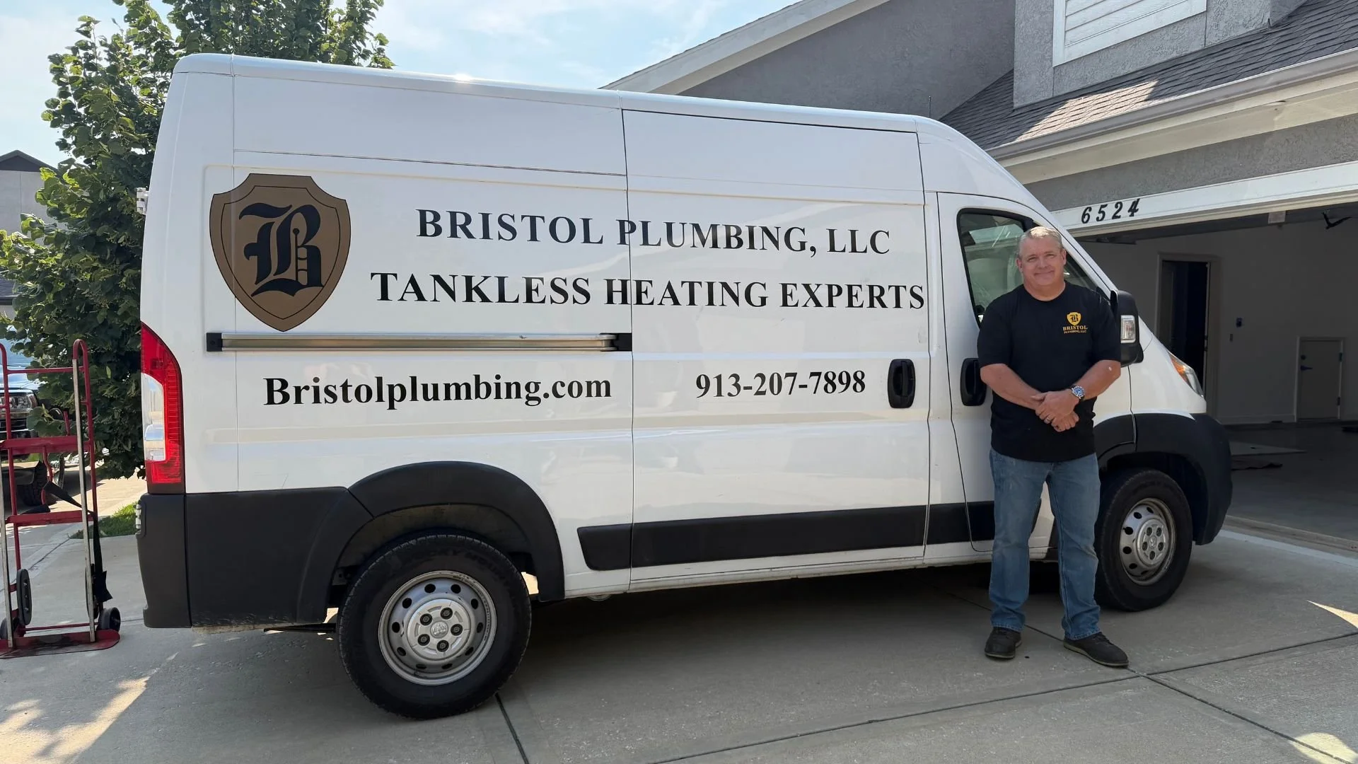Mike Covington of Bristol Plumbing standing in front of white service van with company information and logo on it in driveway of Kansas City home.