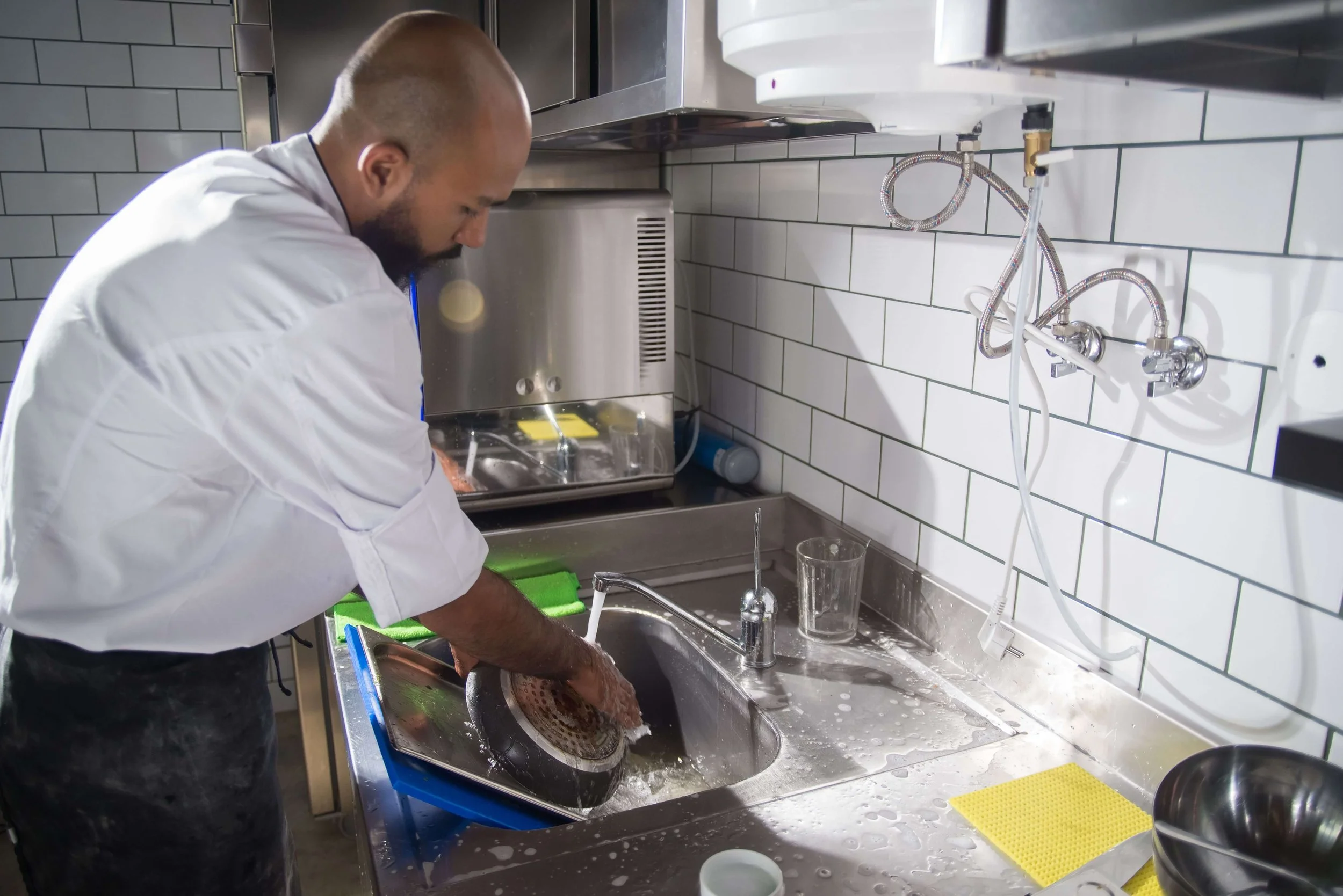 A chef washing a cookware in a commercial kitchen sink.