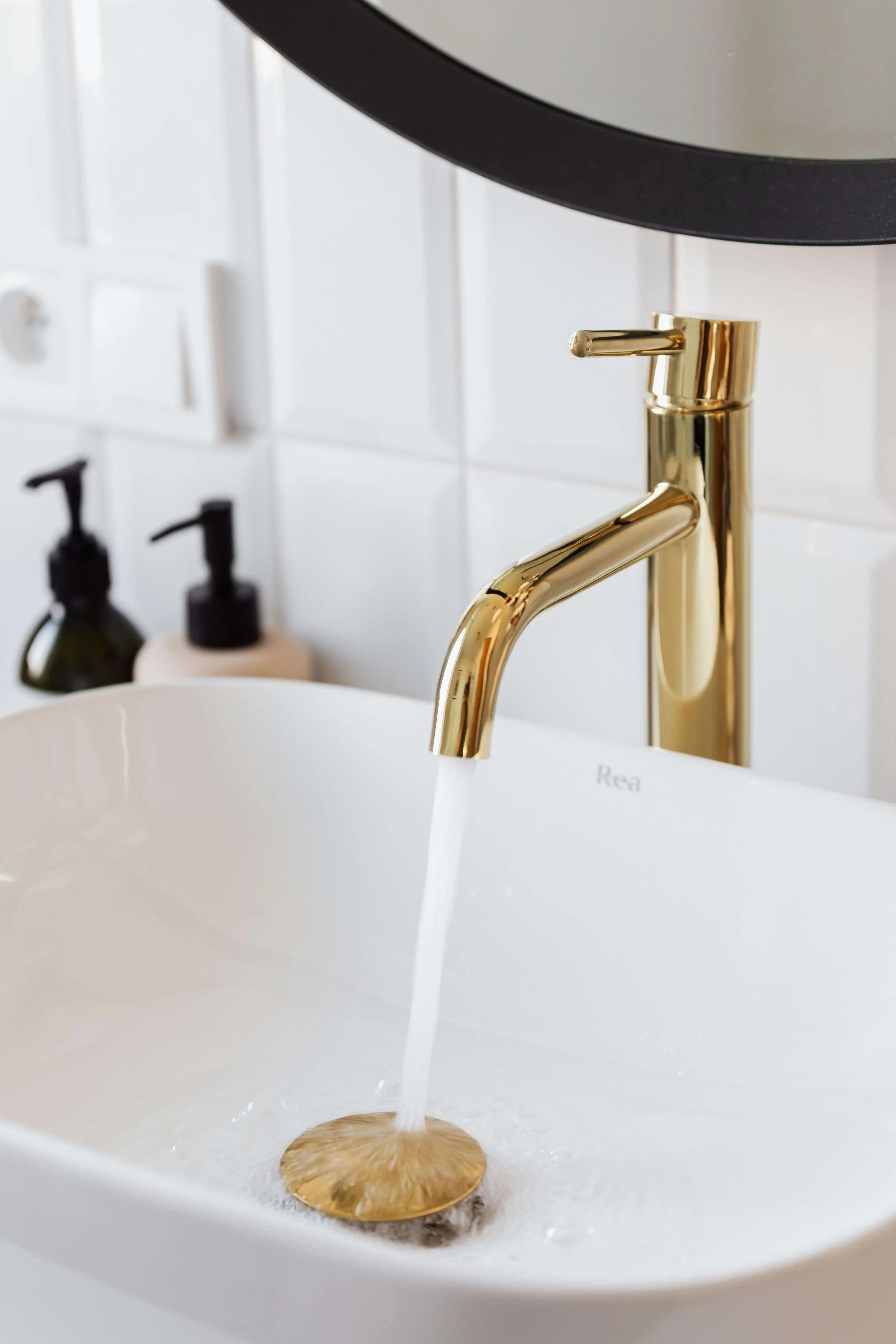 Gold faucet in a white sink with water flowing into a circular gold drain cover.