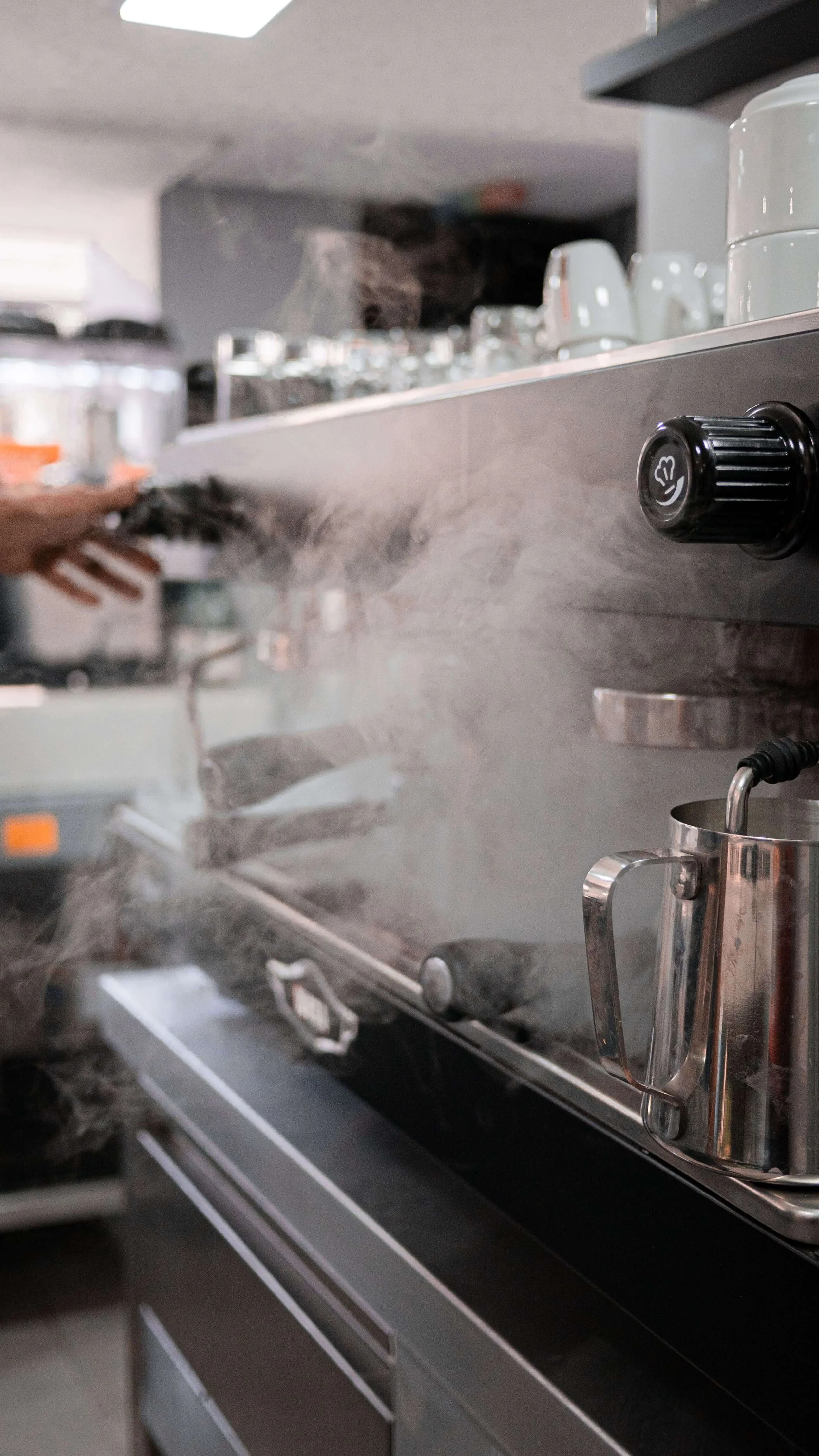 A commercial kitchen stove with a metal coffee pot on the stovetop and a steam cloud rising from it.