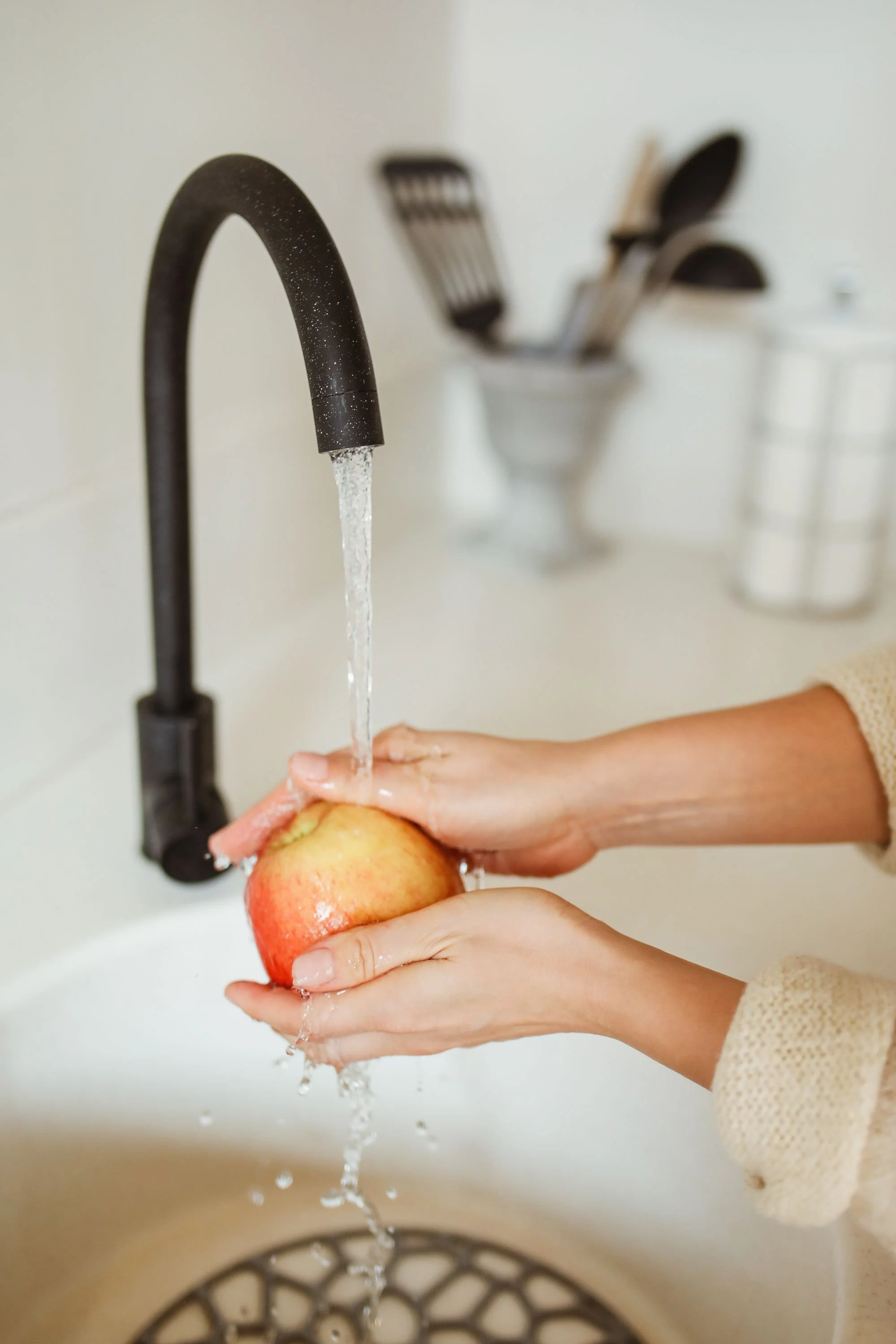 Person rinsing an apple in a kitchen sink under running water.