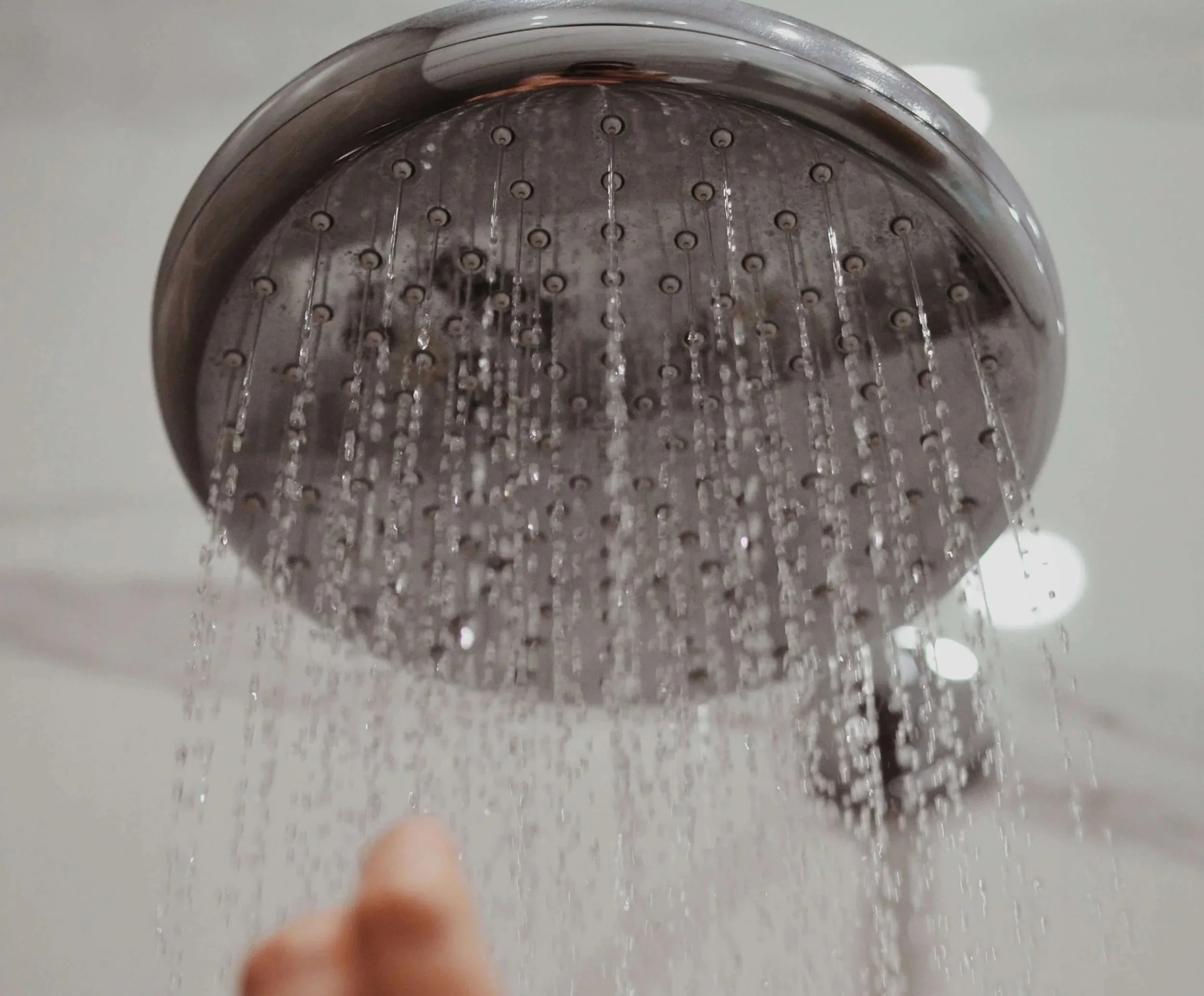 Close-up view of a handheld showerhead with water streaming from multiple nozzles, against a white background.