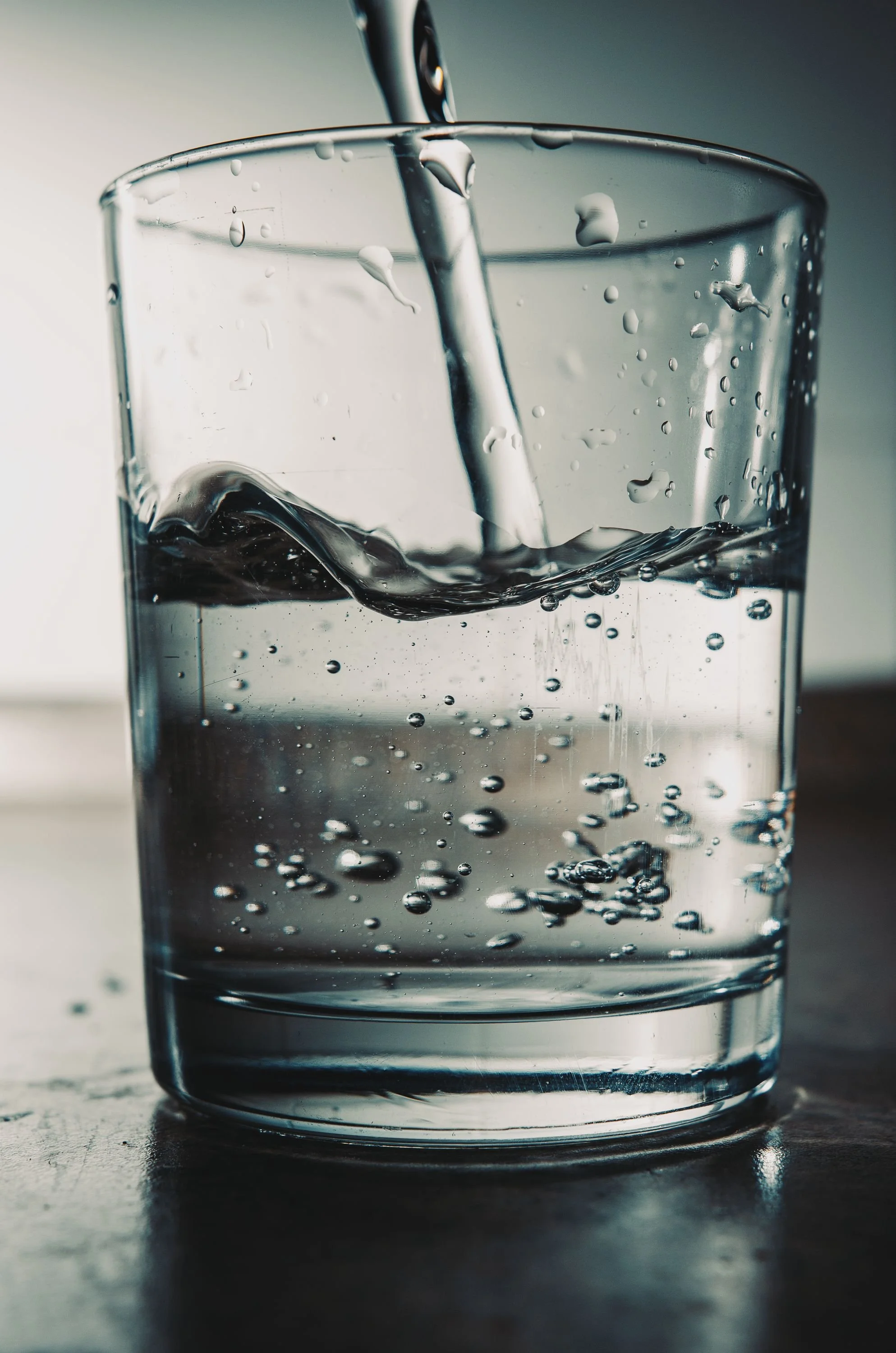 Close-up of a glass with water being poured into it, creating splashes and bubbles.