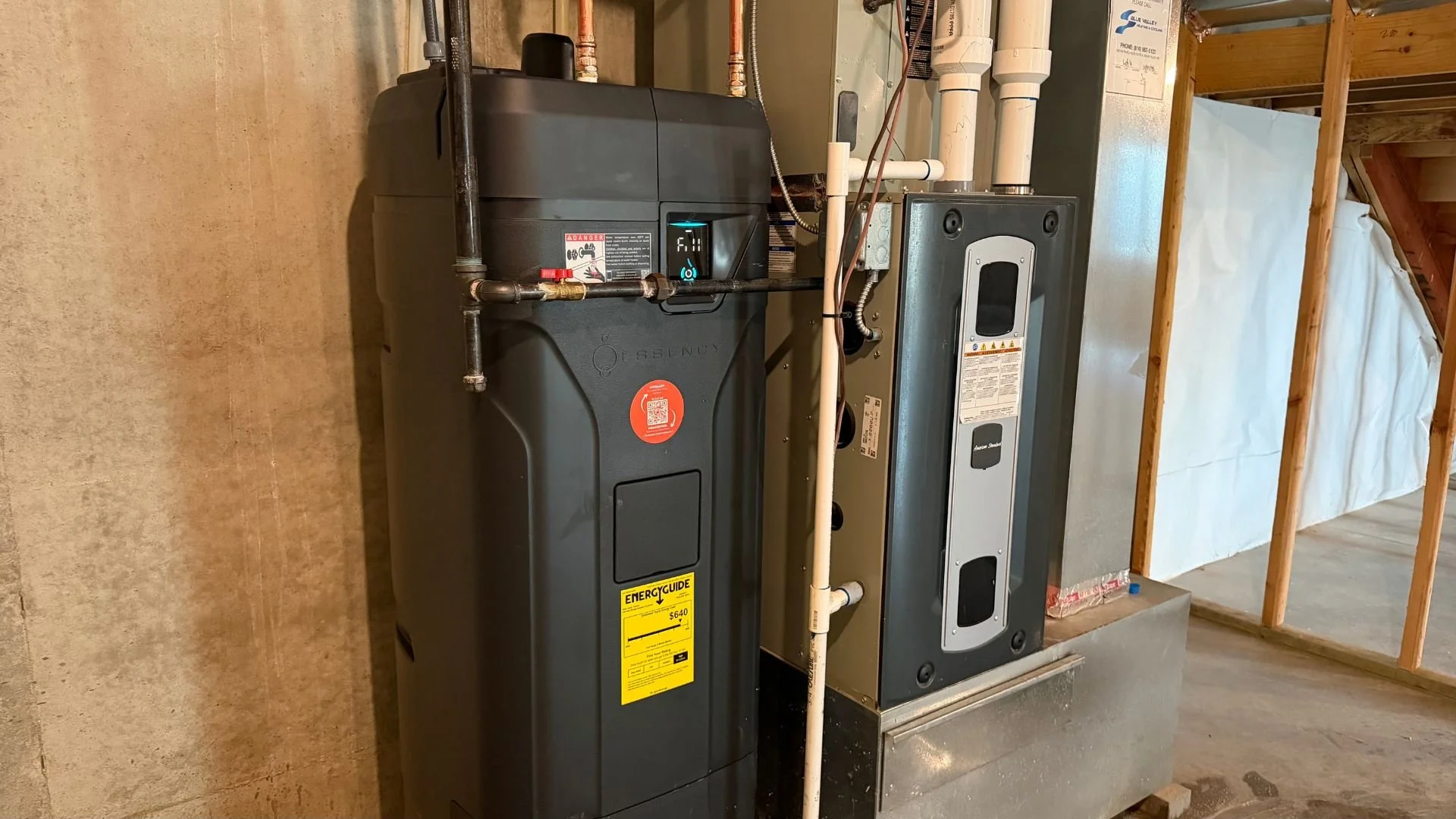 A basement utility area with a high-tech black Essency electric tankless water heater system in a Johnson County, Kansas home.