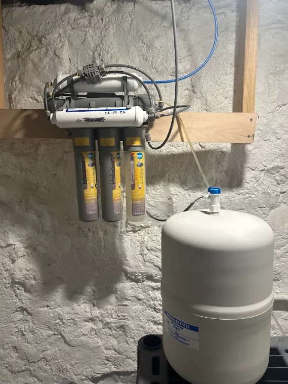 MAC Water Technologies three-stage reverse osmosis drinking water filtration system with gray filters and yellow labels, connected by tubes to a white tank in a utility room in a Johnson County, KS home.