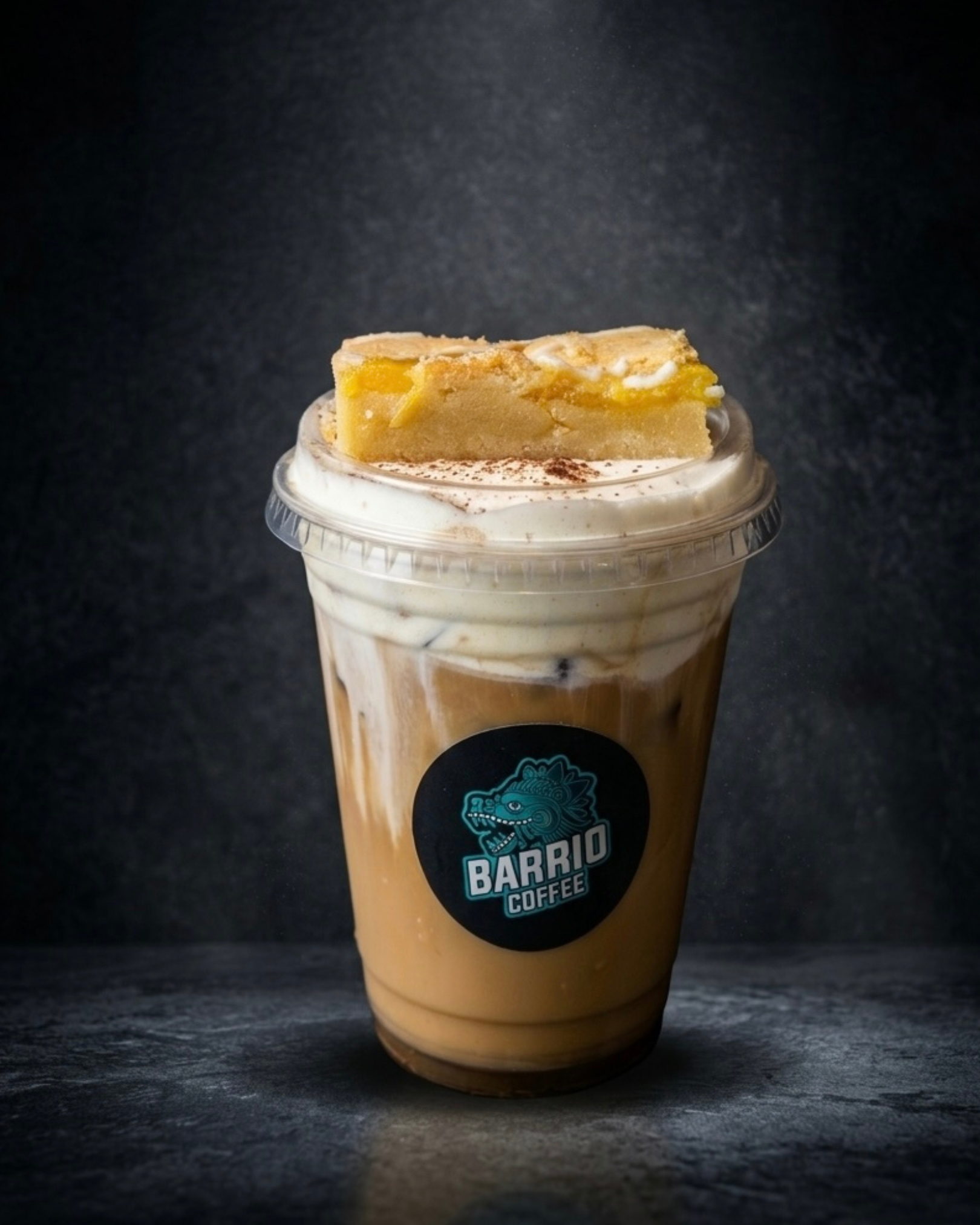 A plastic cup filled with iced coffee topped with a slice of peach and chocolate powder, with a Barrio Coffee logo sticker.