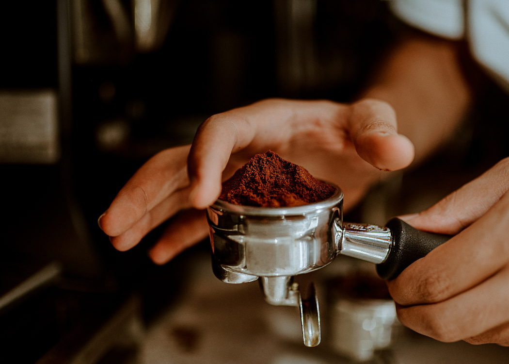 Close-up of person holding a portafilter filled with ground coffee, ready for espresso brewing.