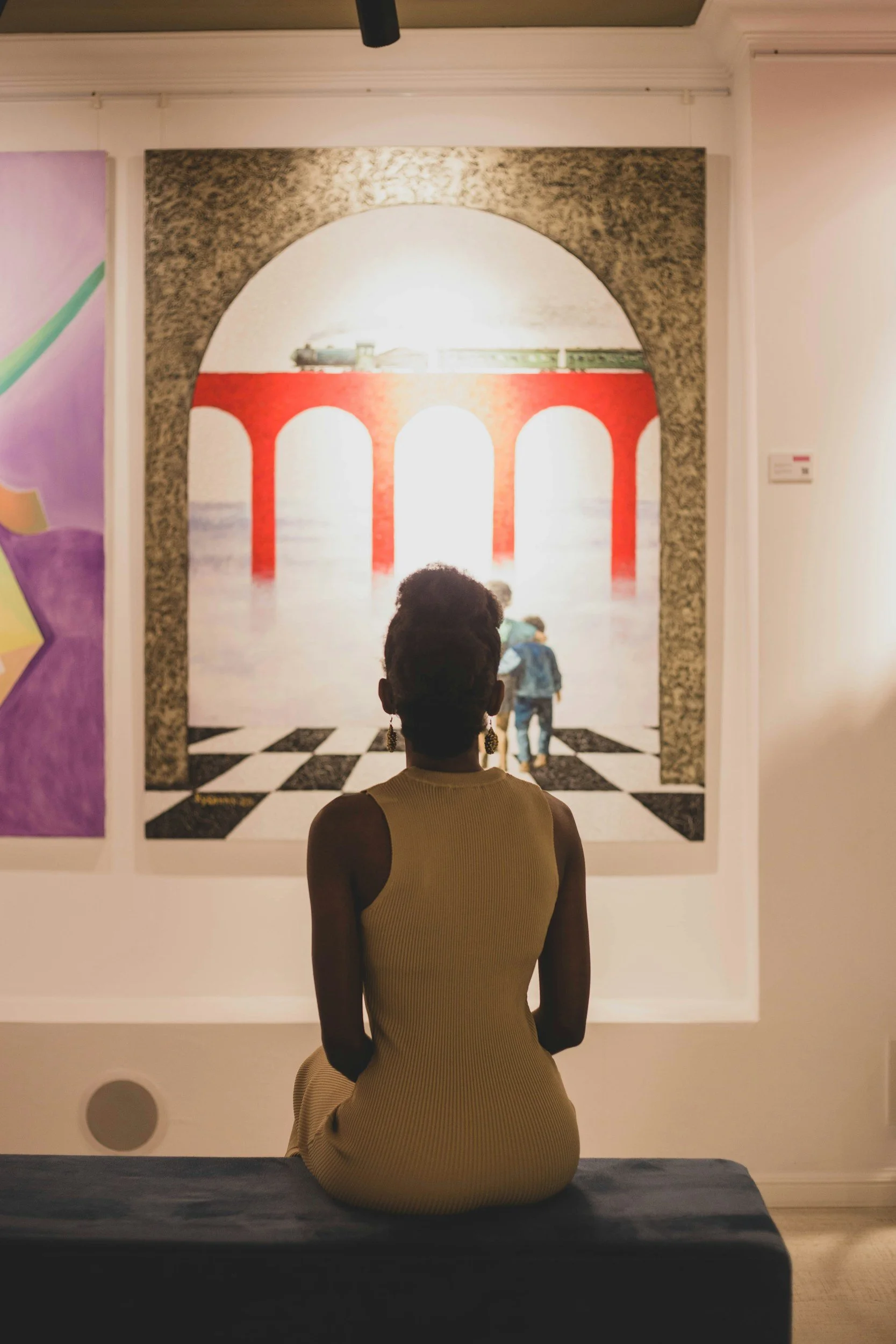 Woman sitting in front of a painting of a train bridge