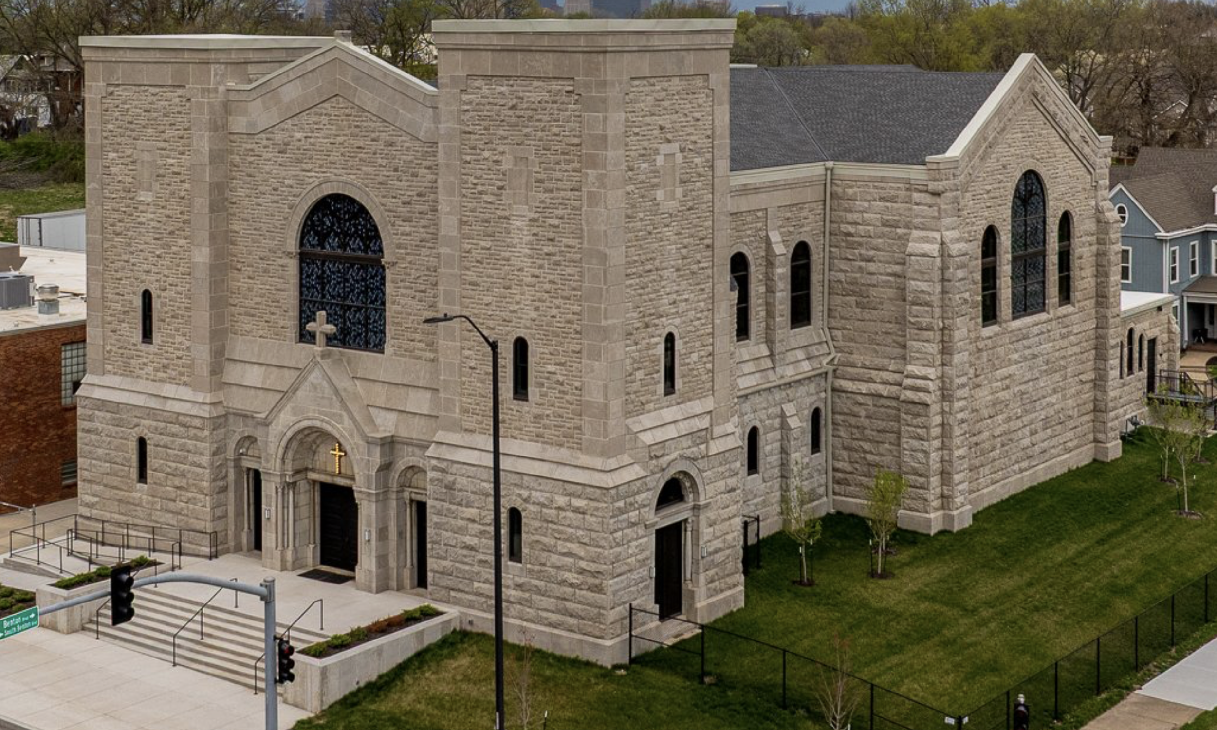 A large stone castle-like event space with arched windows, two towers, and a set of stairs leading to the door. The church has a gray roof and is surrounded by greenery.