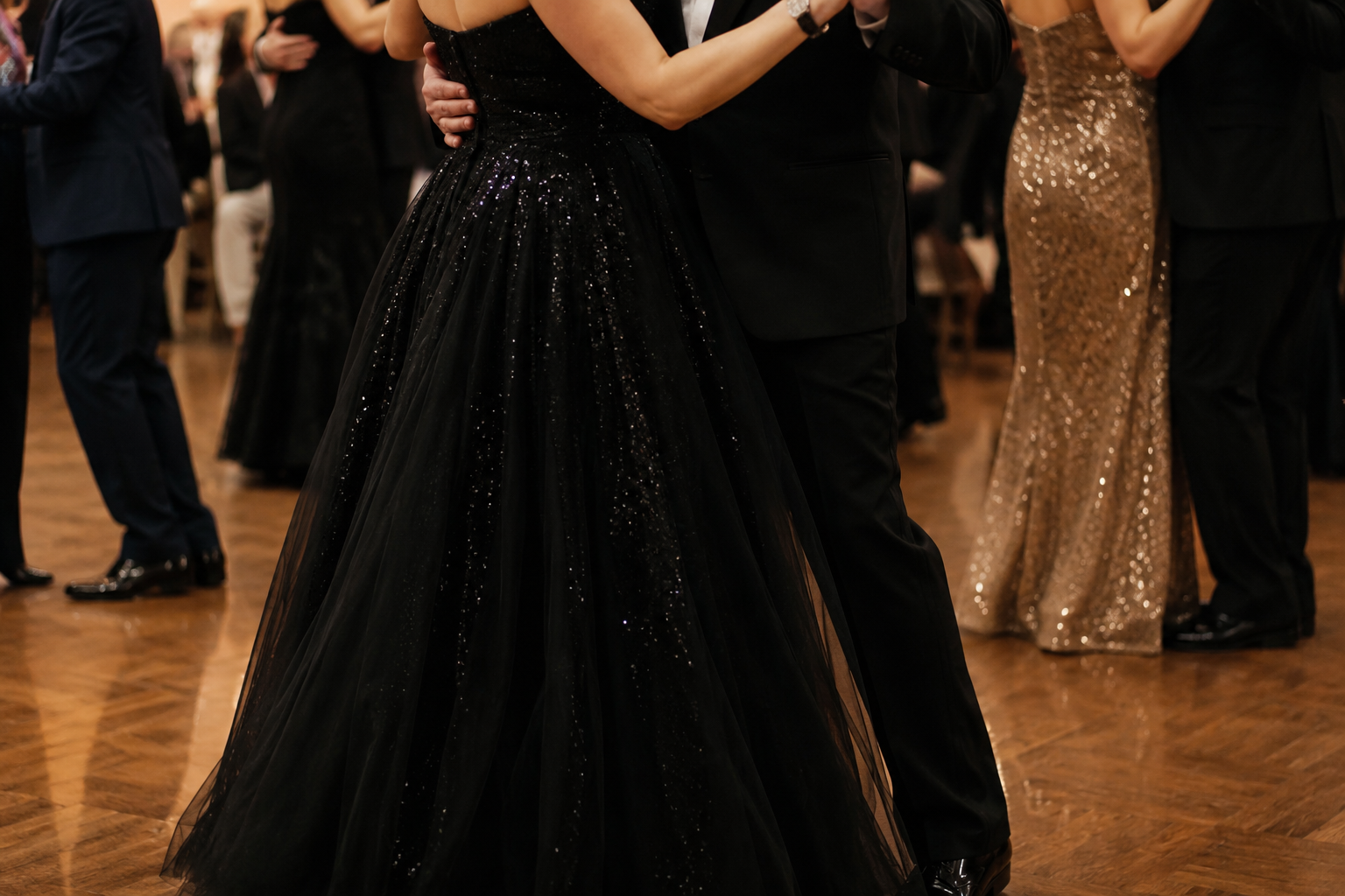 Couple dancing at a formal event, with women wearing glamorous dresses and men in suits, on a polished wood floor.