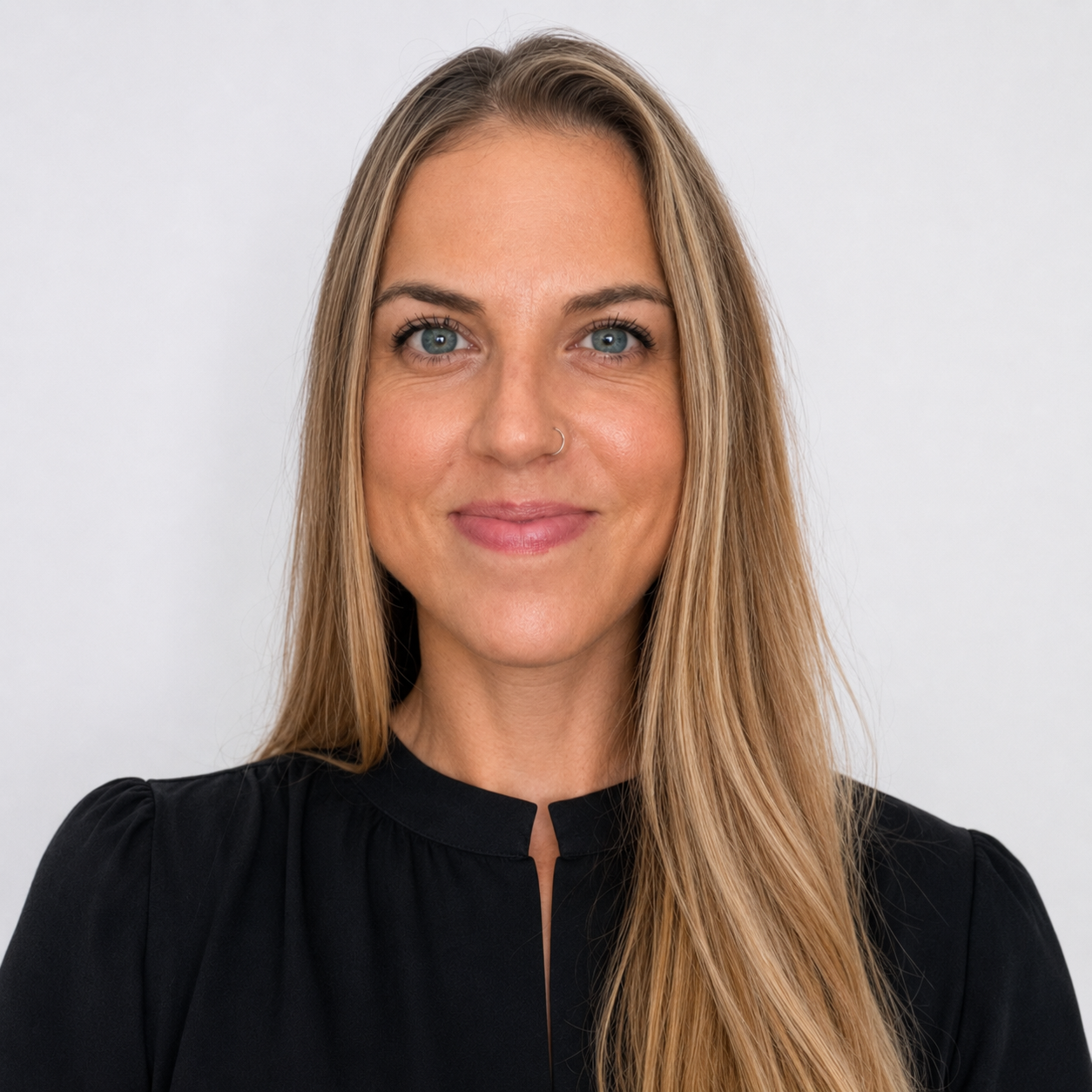 A woman with long blonde hair and blue eyes wearing a black top, smiling at the camera against a plain white background.