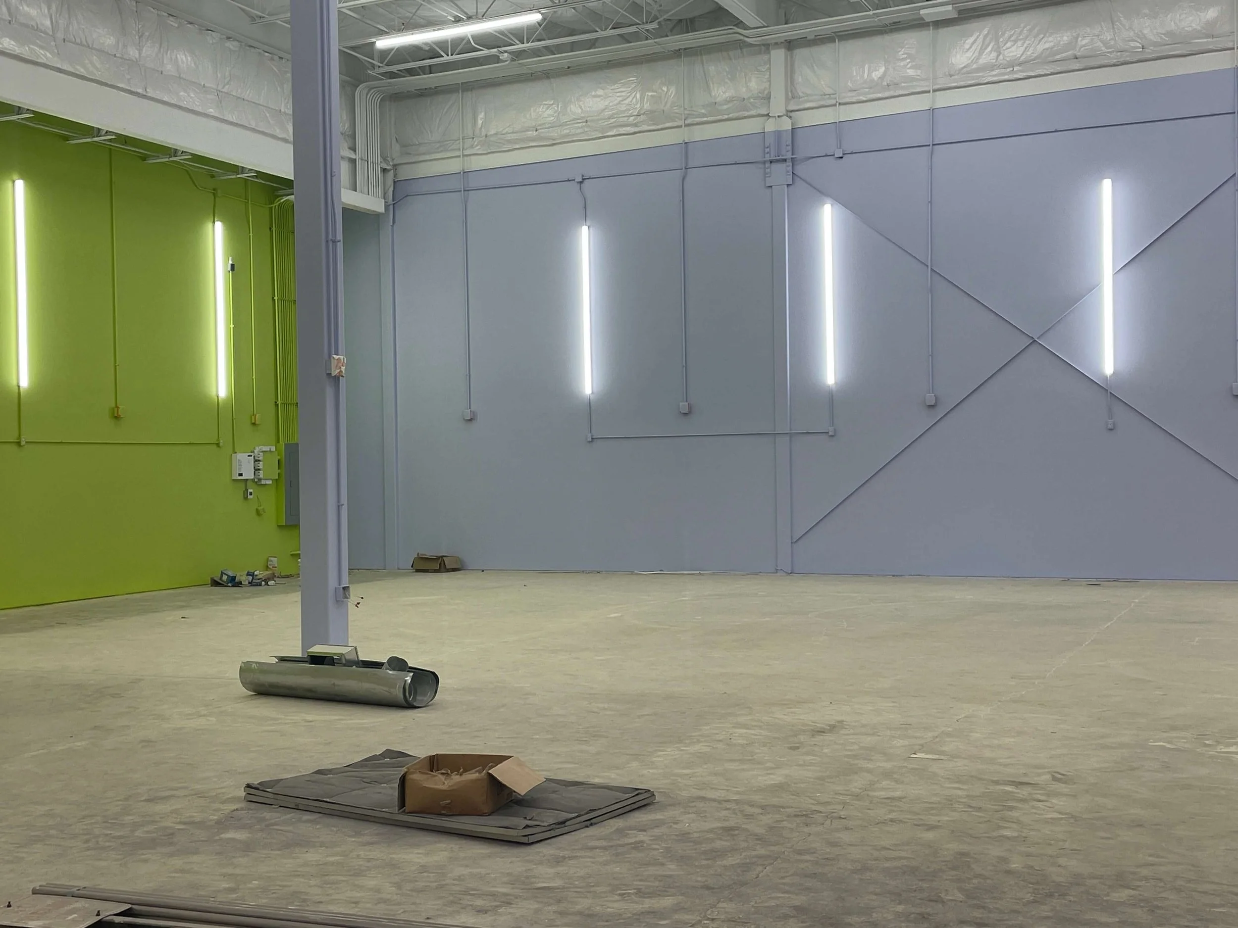 The interior of Kids Empire in Kansas while under construction, a light-blue painted wall and a green wall with light bars on the wall. There is a concrete floor with construction materials on it.