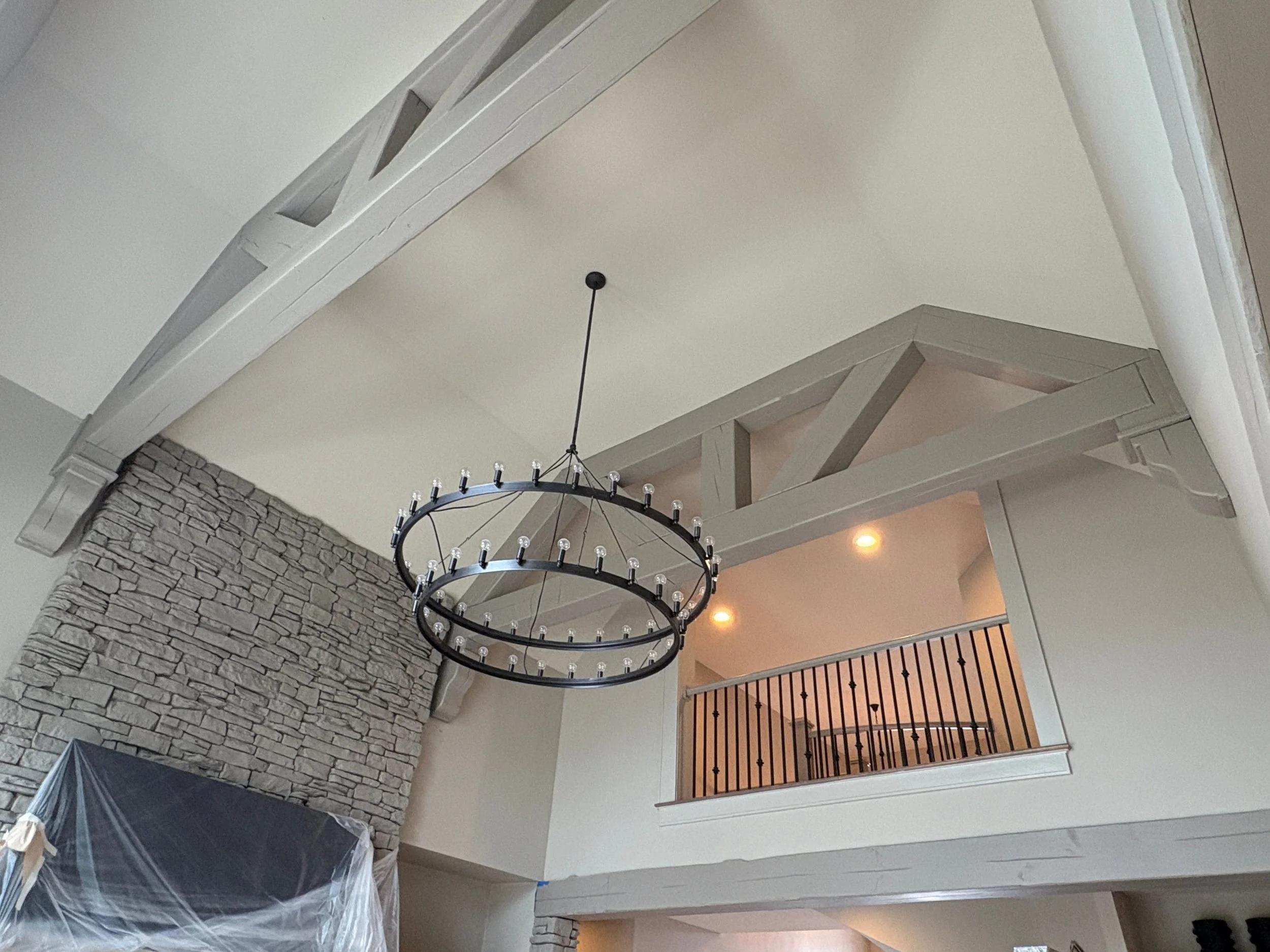 Interior view of a multi-story home with a stone wall, chandelier, and freshly painted gray wooden railings and exposed beams.