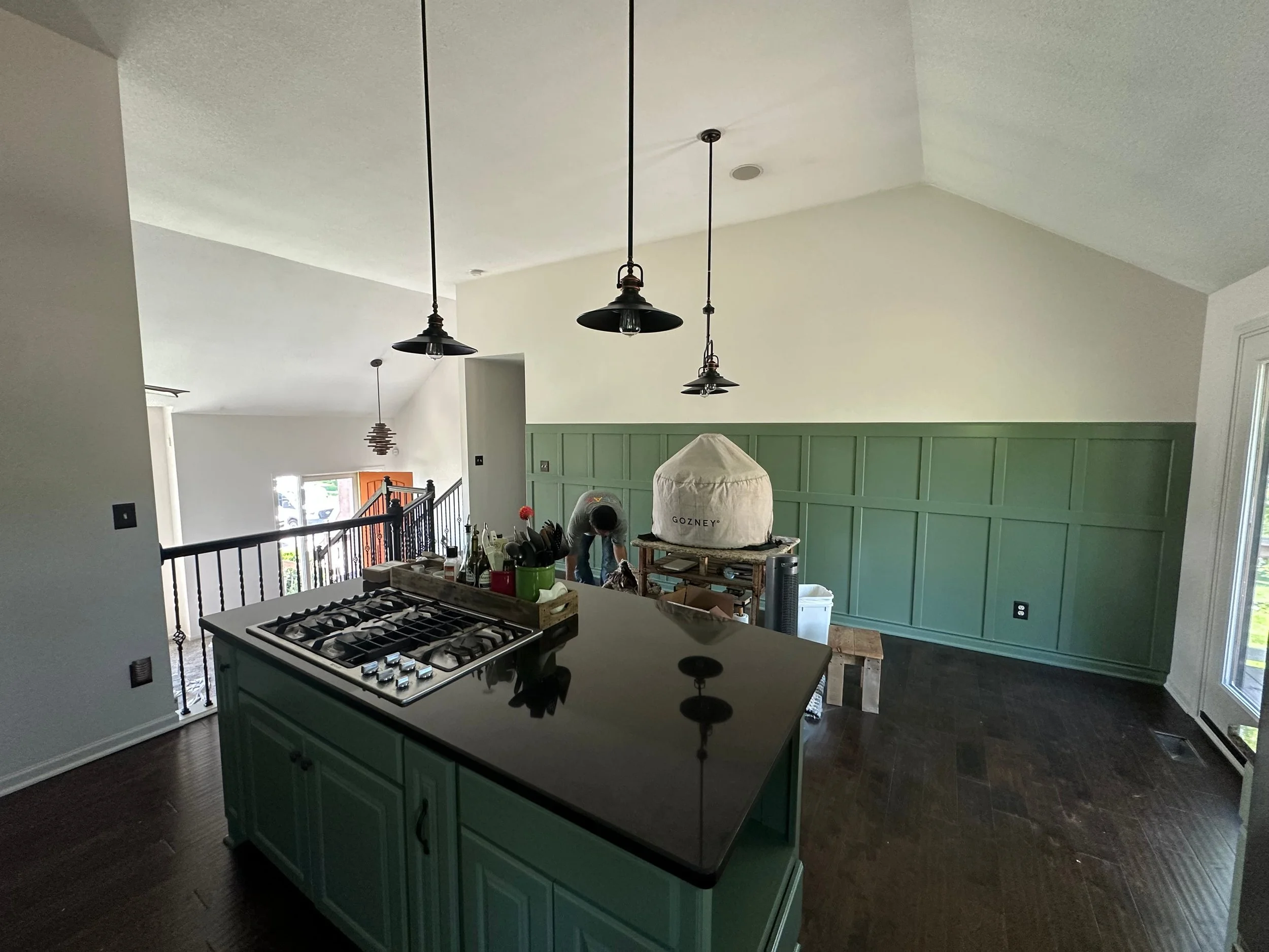 Kitchen in Johnson County, Kansas home with a black kitchen island and pendant lights with a newly painted far wall with green beadboard on the bottom half and a white top half of the wall and a white steepled ceiling.