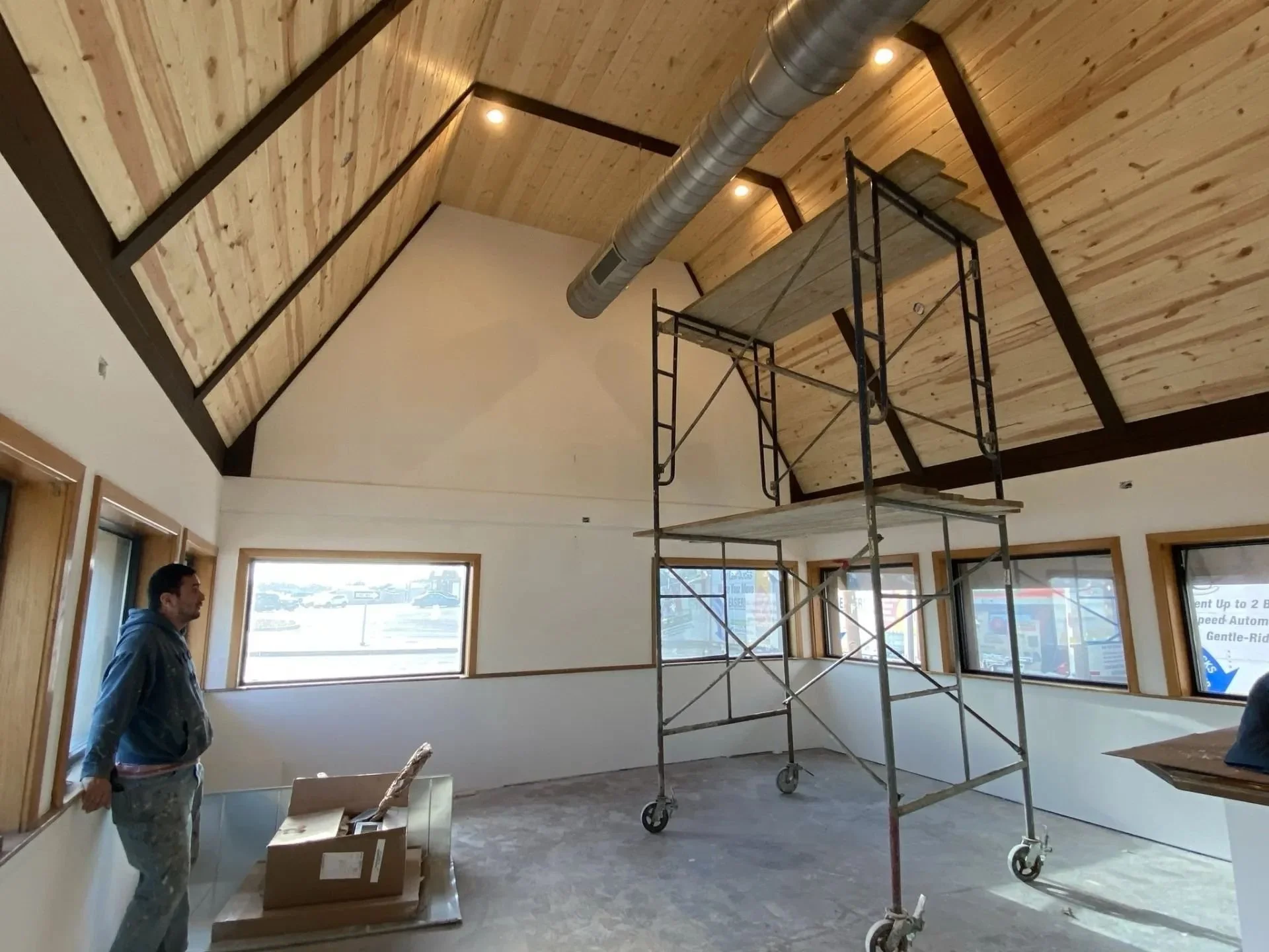 Interior of a building with wooden ceiling, scaffold, and windows, an LAK Painting painter standing near the wall with construction materials on the floor.