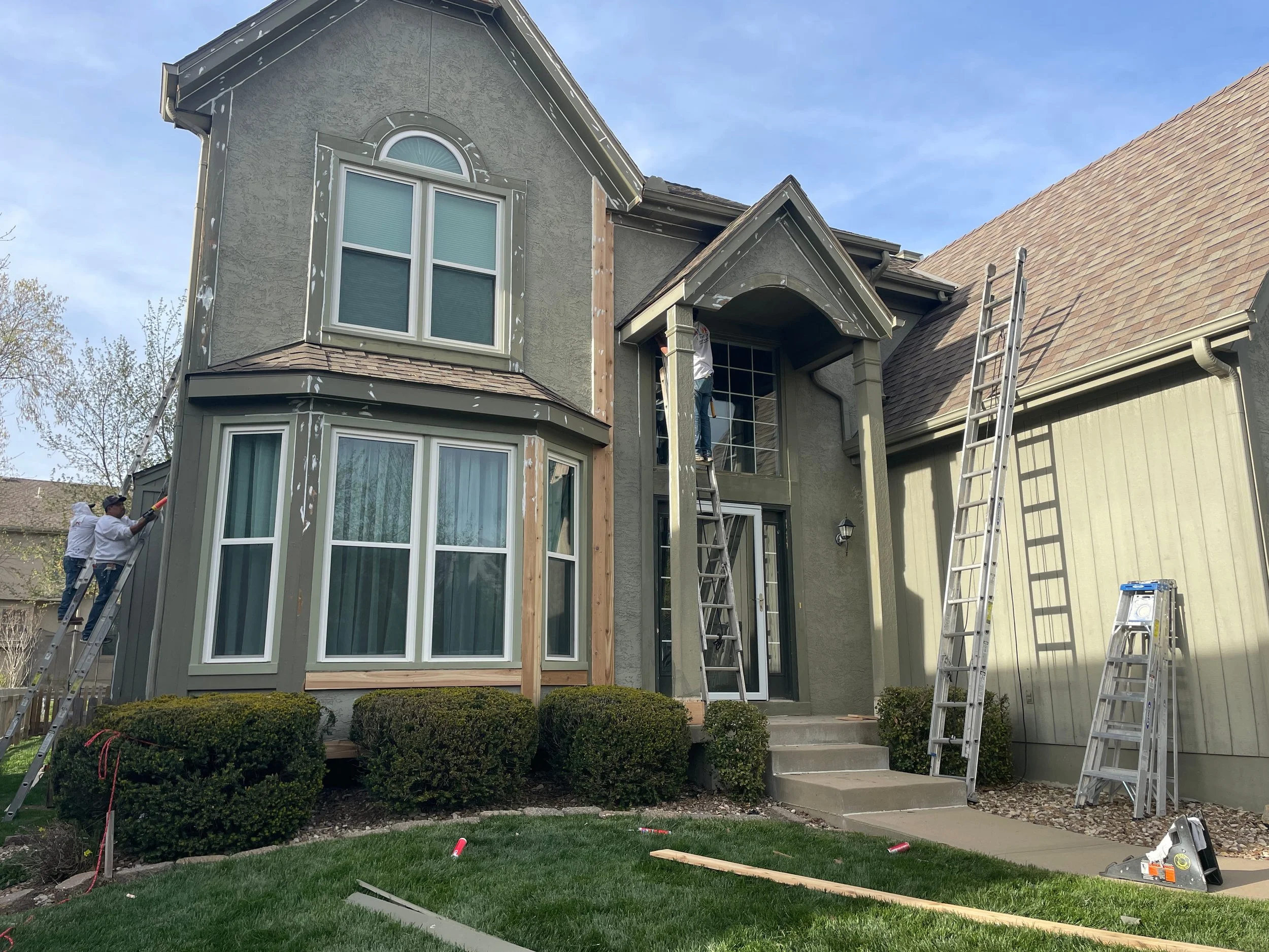 The exterior of a residential house in Kansas City with wooden trim removed. Ladders and tools of LAK Painting are positioned around the house.