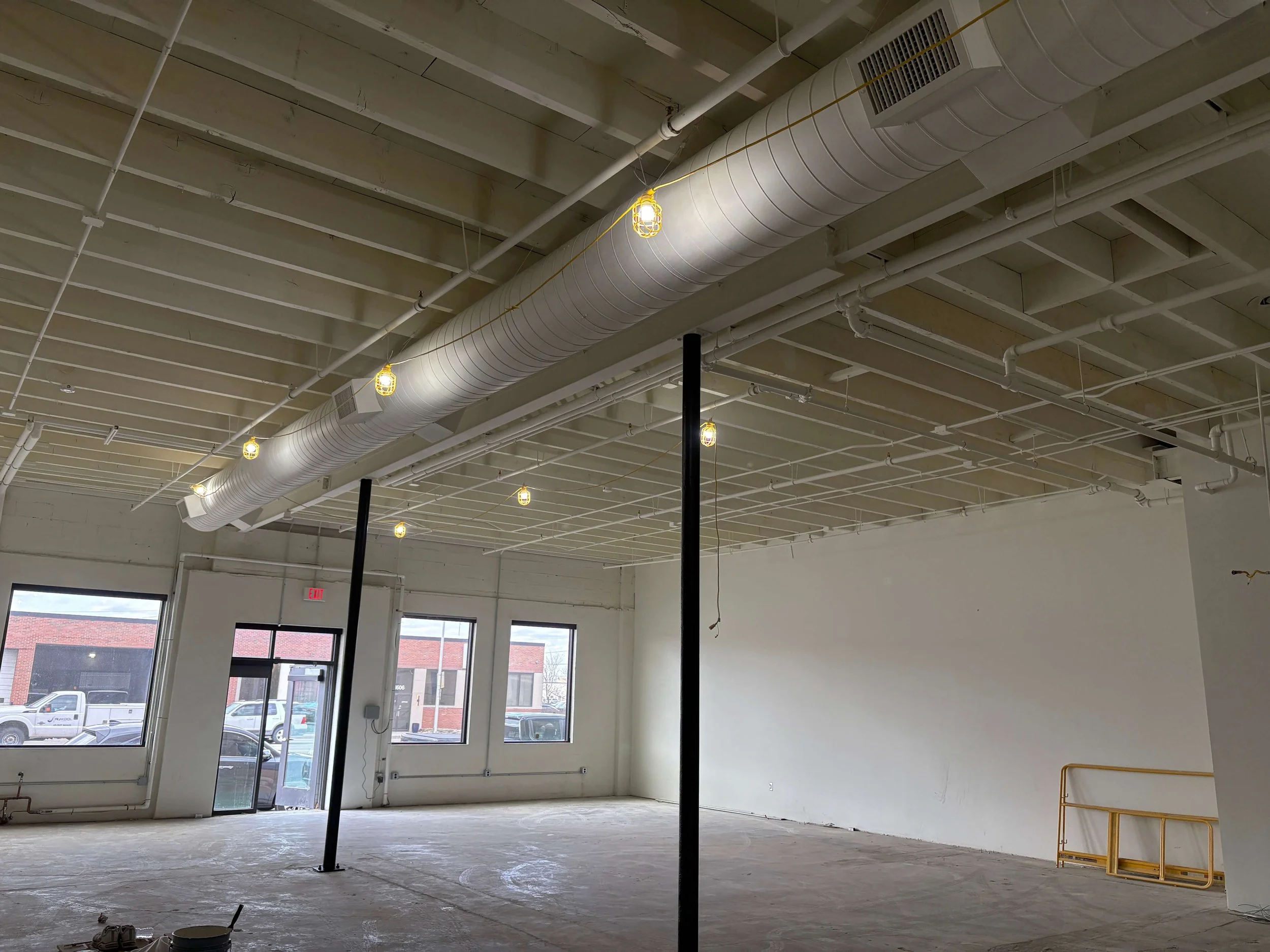 ACI Gym newly painted white by LAK Painting in Kansas while under construction with high ceilings, exposed ductwork, and scaffolding. The walls are white and there is a concrete floor with two black structural posts.