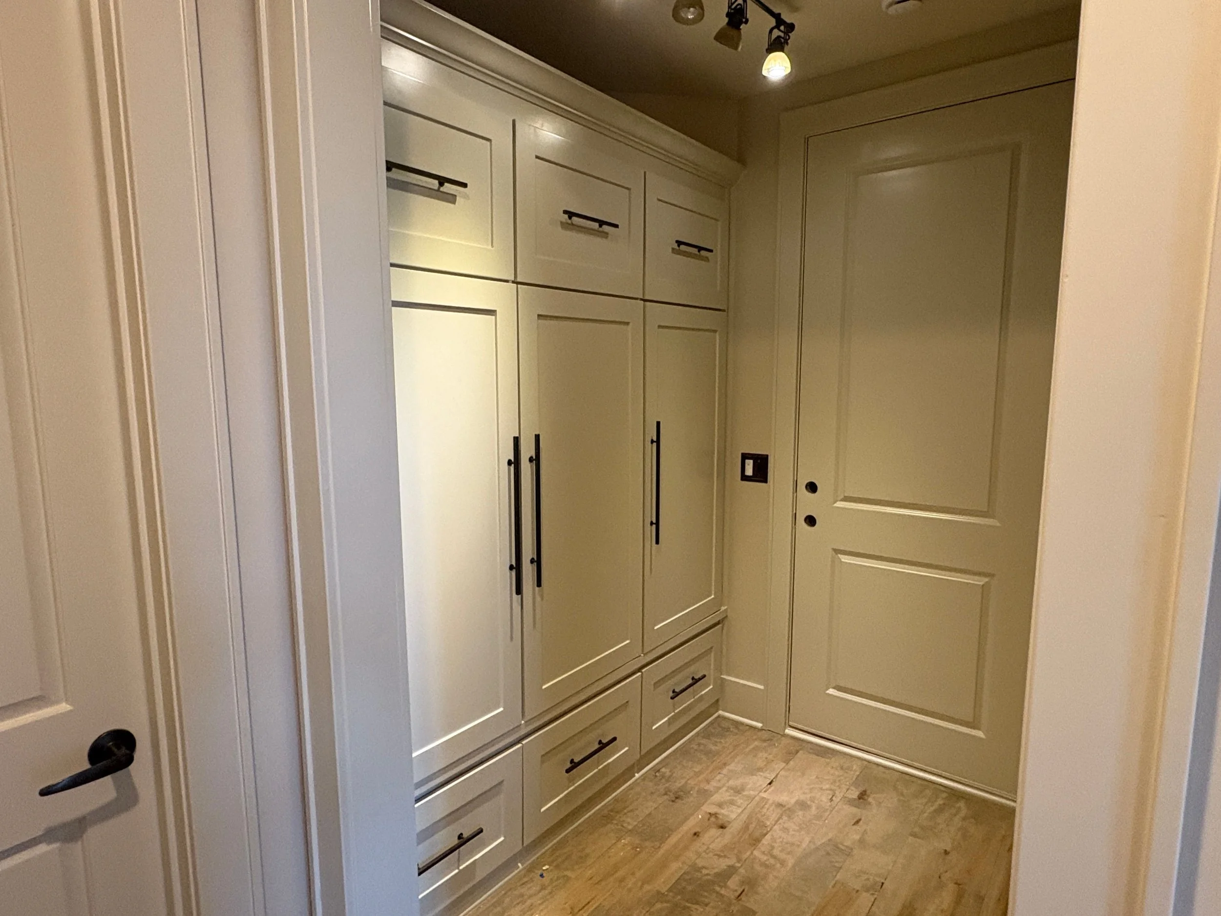 Interior view of beige closet and pantry doors with multiple drawers, black handles with wood flooring.