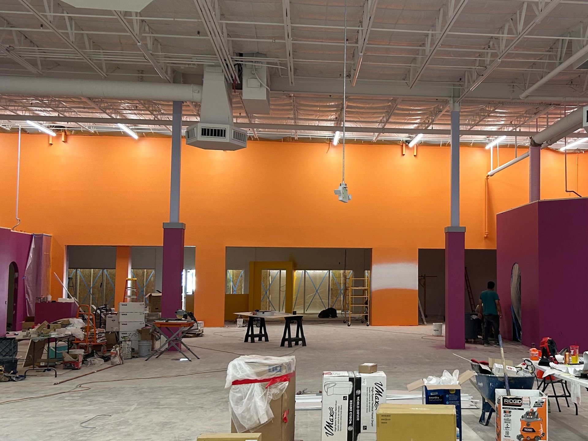 The interior of Kids Empire in Kansas while under construction. The far wall is bright orange with the right wall and structural beam-guards painted purple. There is construction materials in the center of the room.