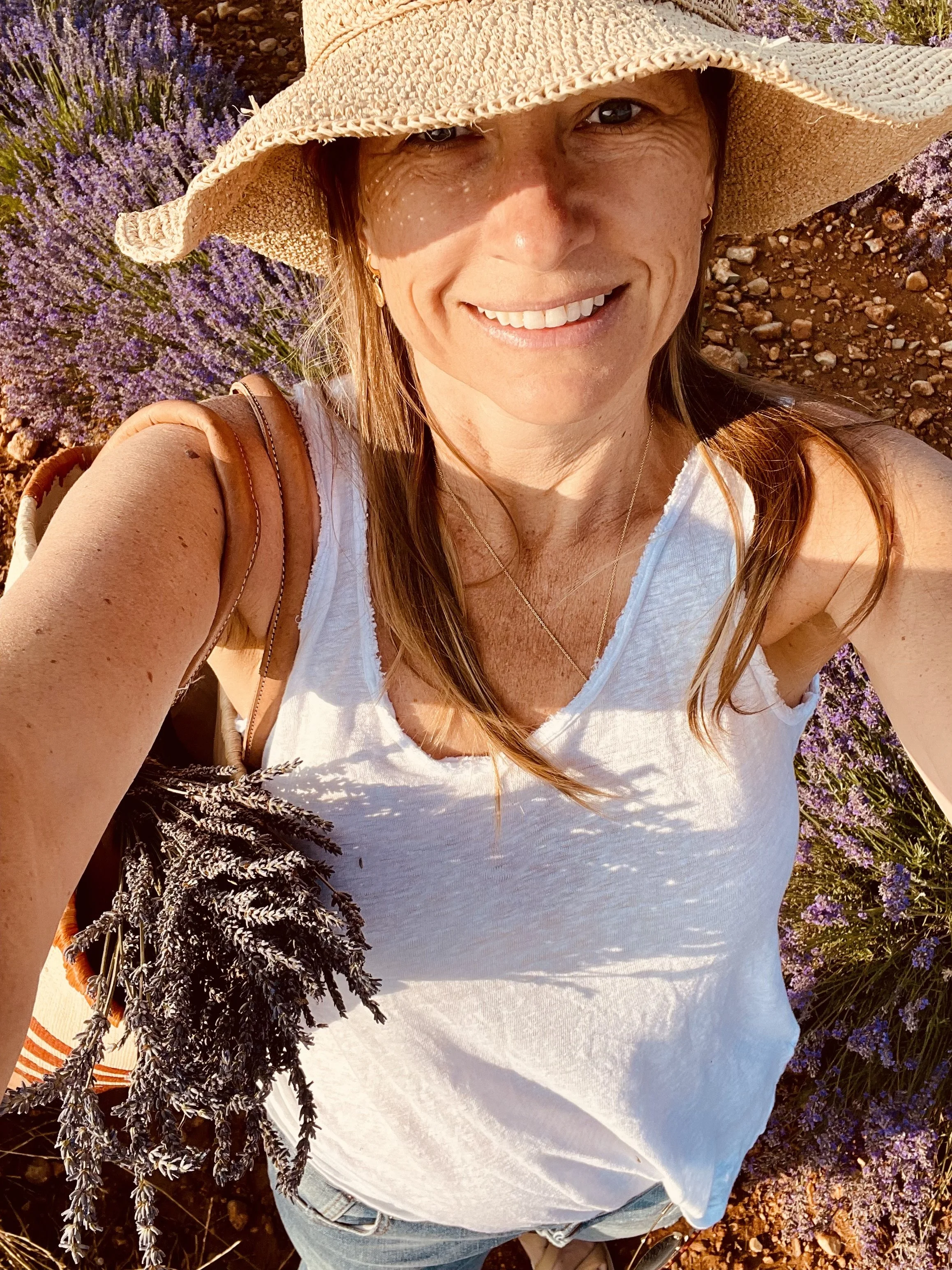 Woman smiling in a field of lavender, wearing a sun hat.