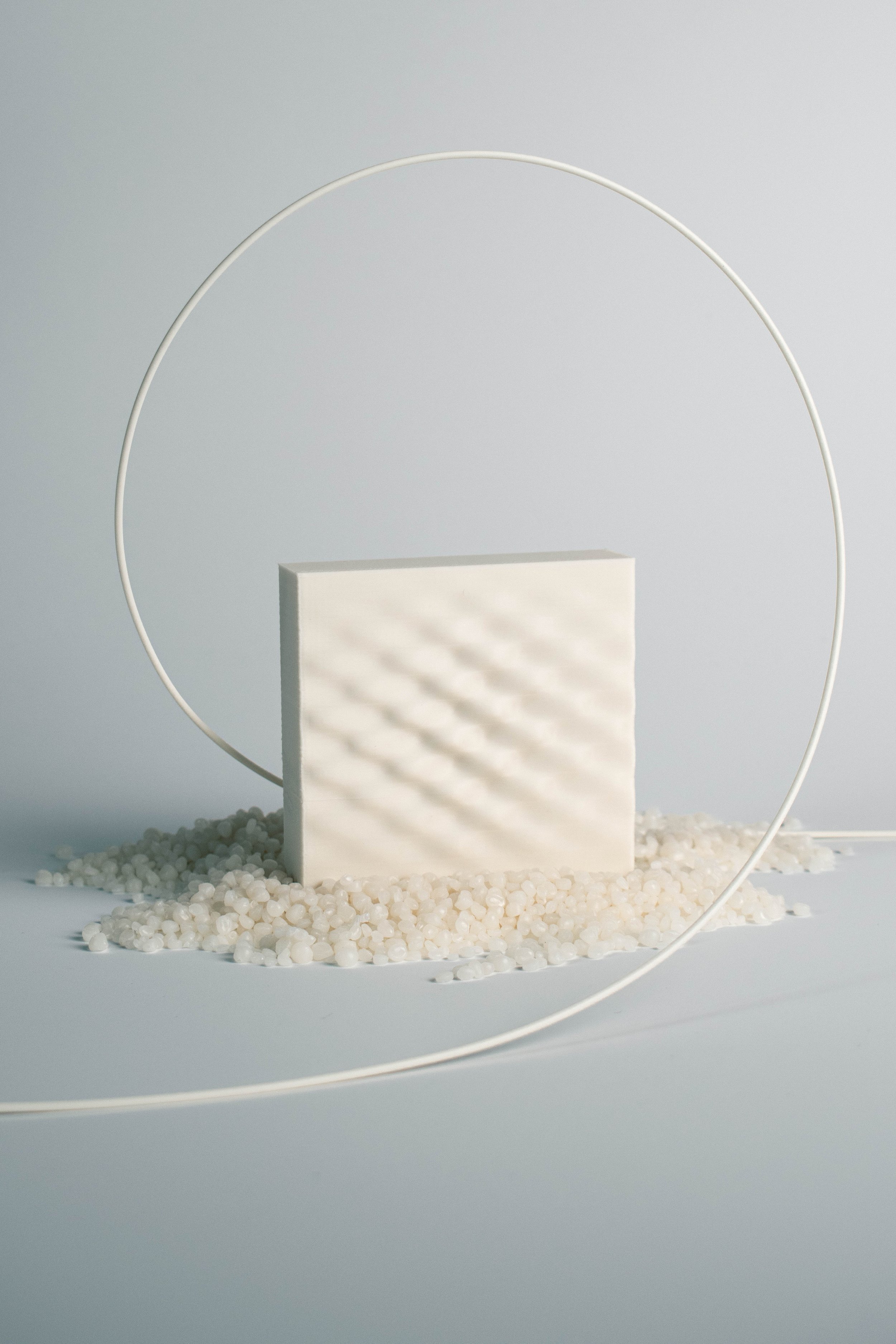 Shell White 3D-printed surface sample encircled by filament above pale material pellets