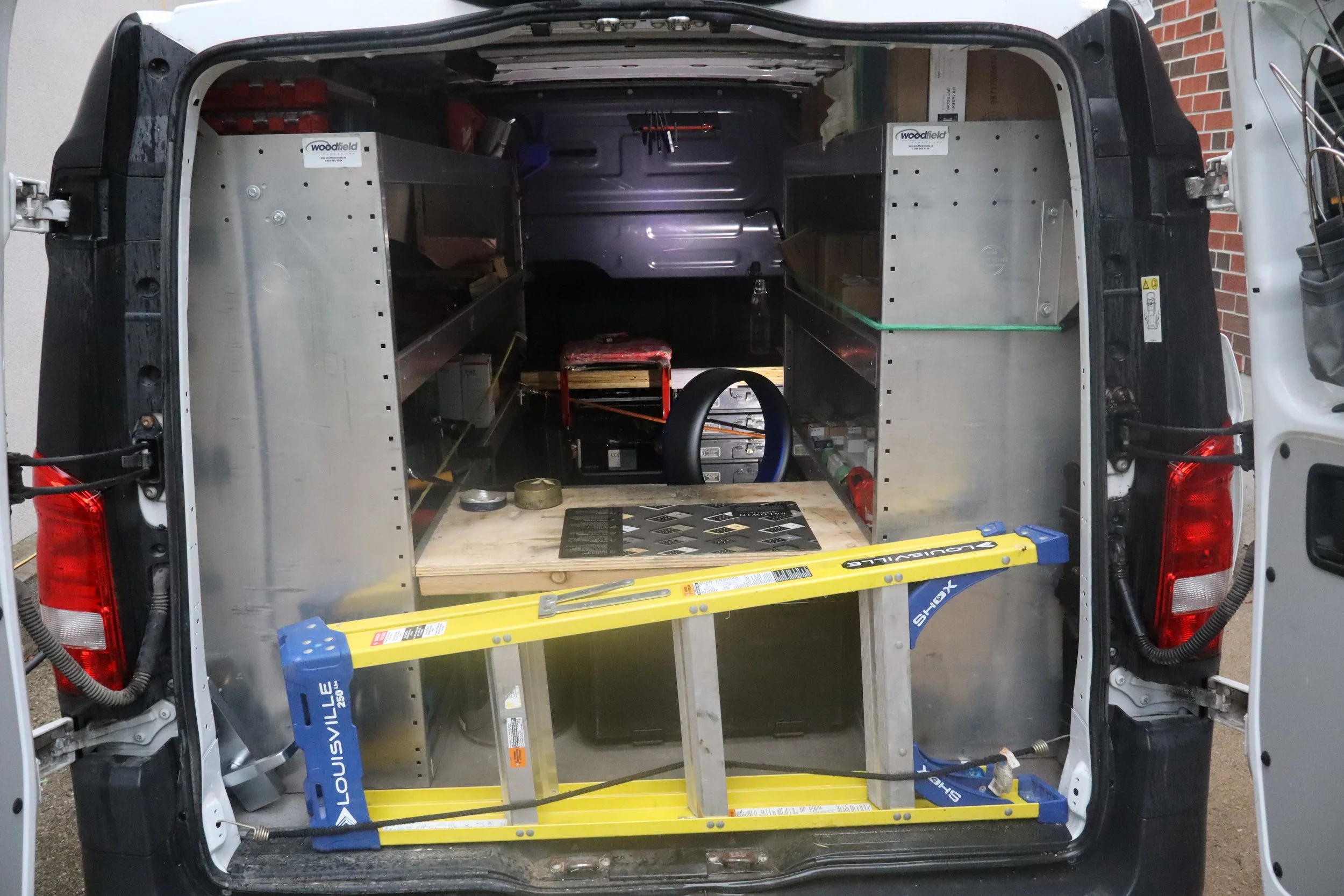 Back of a van with partial interior view showing metal framework, tools, a yellow level, and a workbench inside.