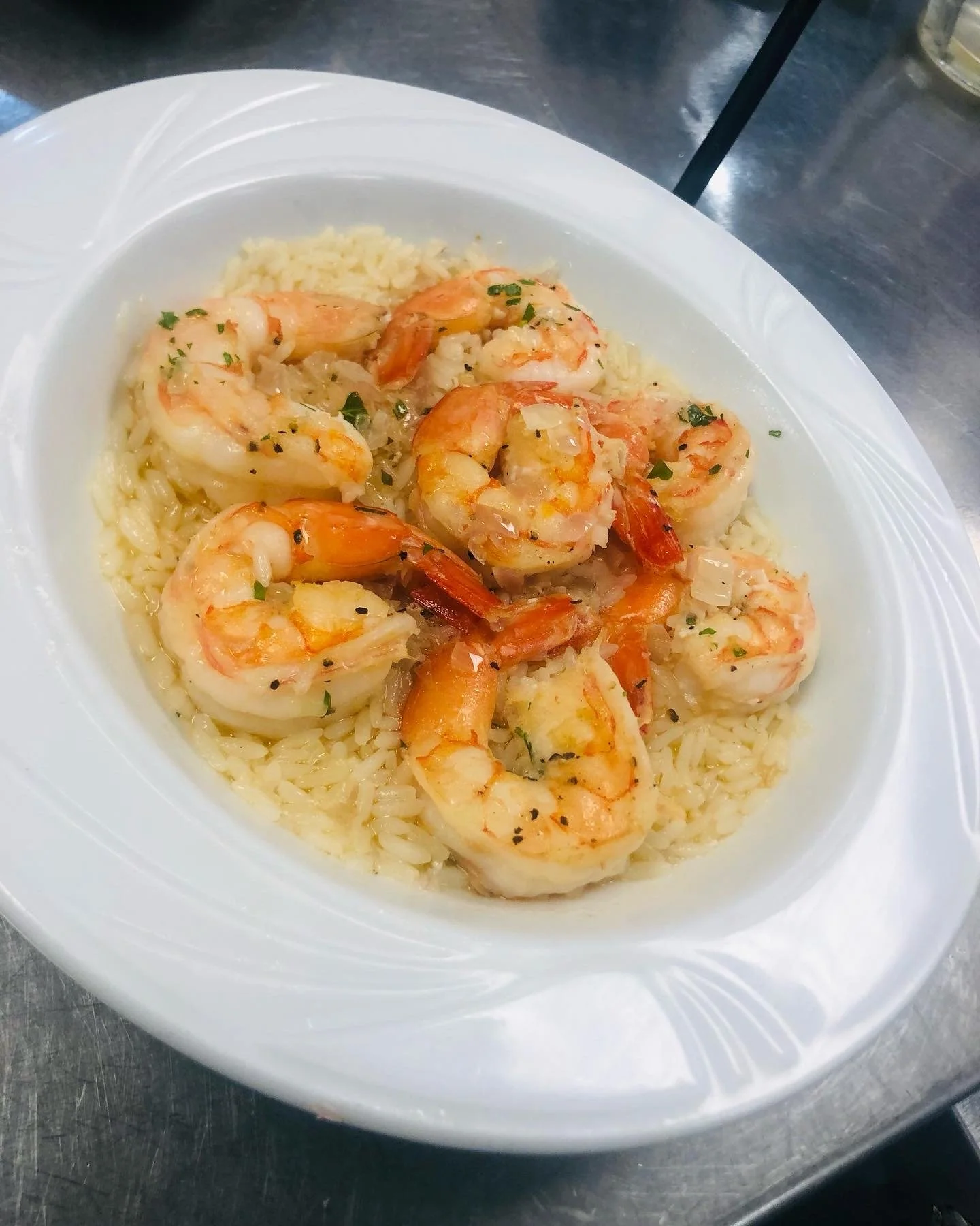 A white plate with cooked rice and a serving of cooked shrimp garnished with chopped herbs.