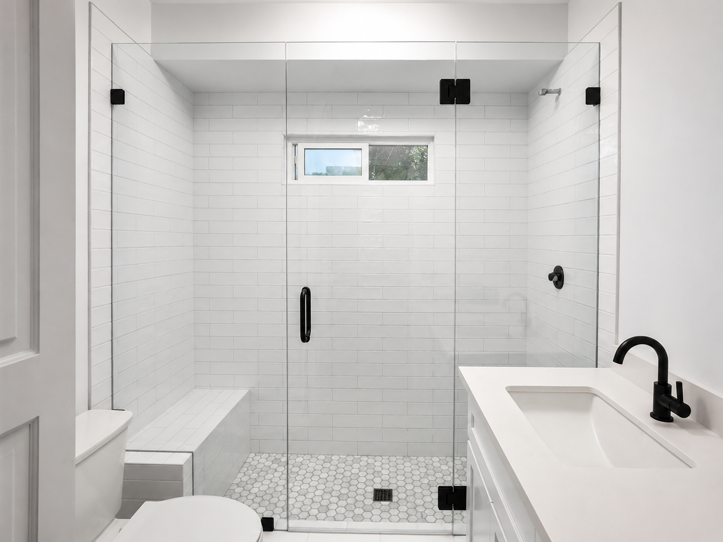 Three-panel frameless shower enclosure with matte black hardware, right-side hinged door, fixed glass panels, and a full-width marble bench.