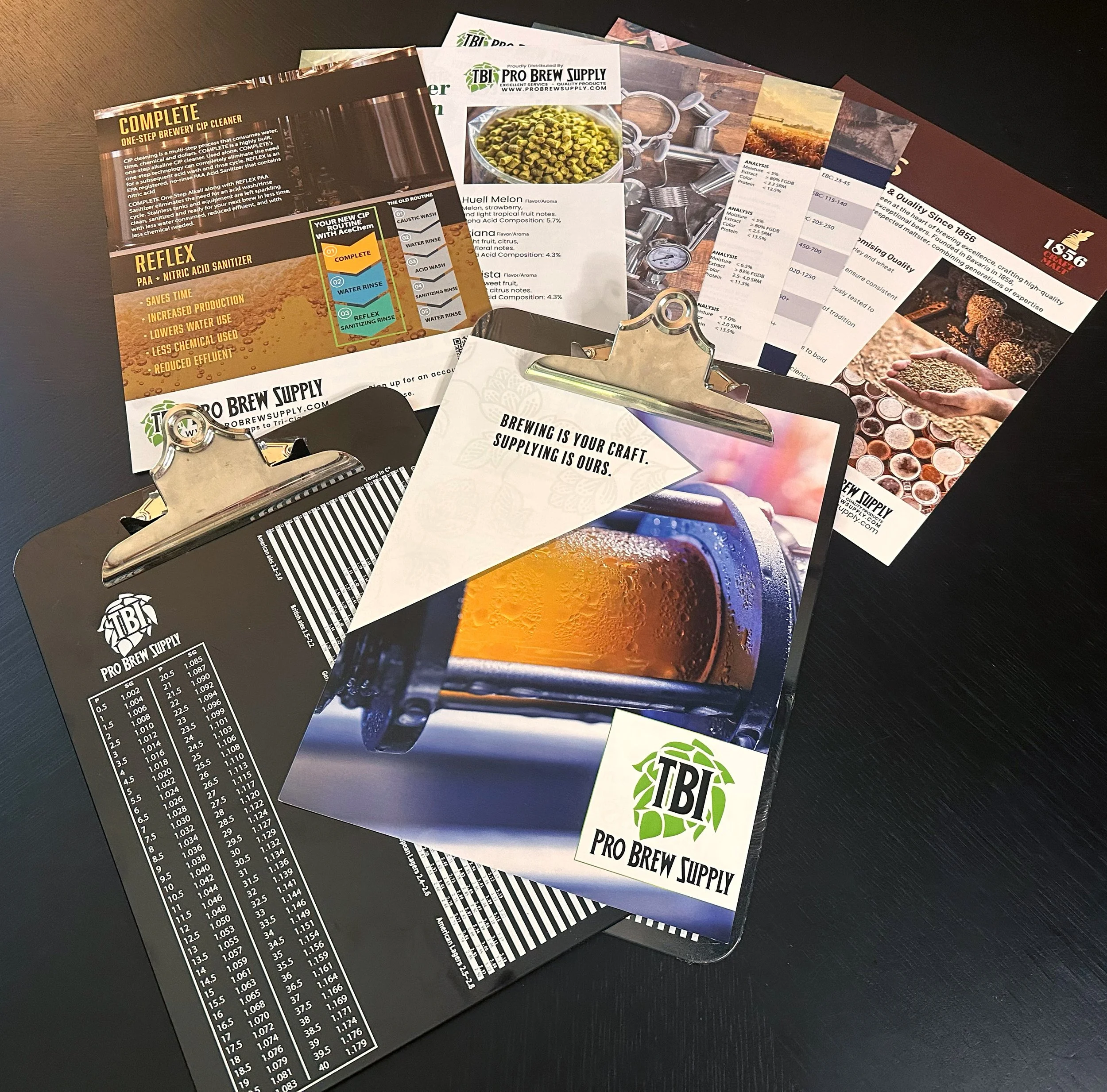 Various printed materials on a dark surface, including brochures and flyers from Pro Brew Supply, featuring brewing products, guidelines, and colorful images of grains, hops, and beer.