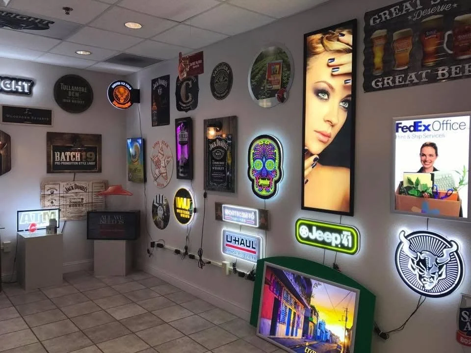 A room with various illuminated signs and posters on the walls, including a large poster of a woman with makeup, neon signs, and advertisements for brands like FedEx, Jeep, and Jack Daniel's.