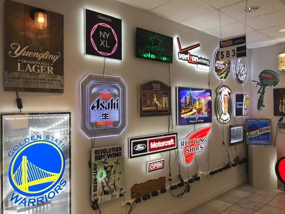 Wall decorated with various illuminated beer and brand signs, including Asahi, Heineken, Bud Light, Red Wing Shoes, Ford, and Golden State Warriors, in a restaurant or bar setting.