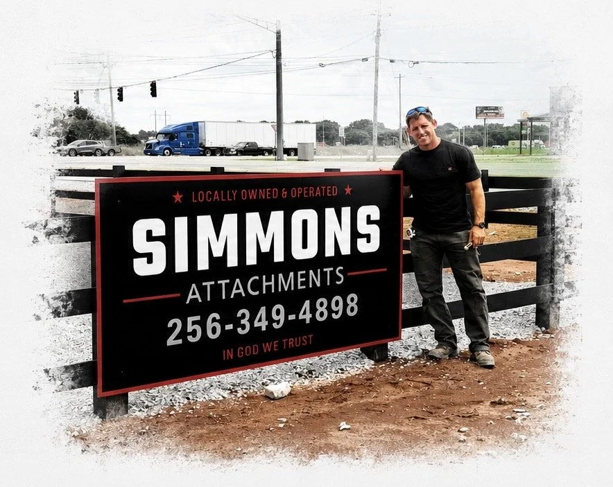 Man standing next to a sign for Simmons Attachments, a locally owned and operated business, with a phone number 256-349-4898, outdoors near a road with vehicles and power lines
