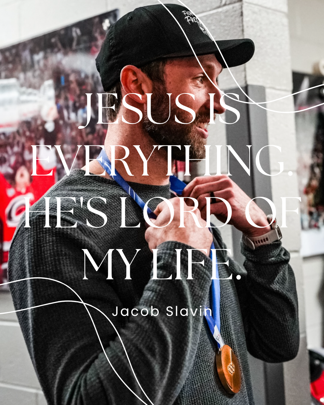 A man in a black cap and gray jacket adjusting a blue medal with an orange pendant around his neck. The background shows a blurred crowd and event posters. Overlaid text says, 'Jesus is everything. He's Lord of my life.' by Jacob Slavin.