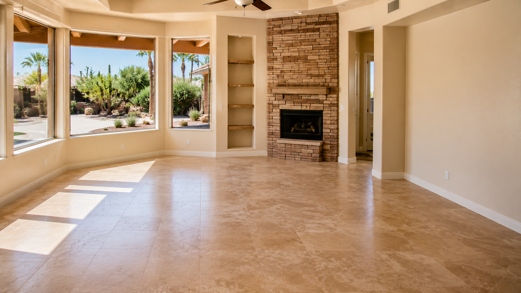 Empty living room with large windows, brick fireplace, built-in shelves, tiled floor, and view of desert landscape outside.