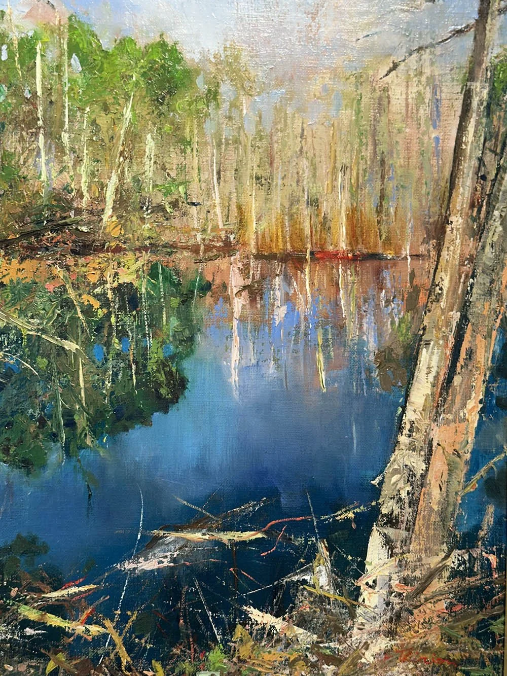 A landscape scene featuring a calm river with reflections of trees and foliage along the banks, vibrant greenery on the left, and a mix of trees on the right with shadows cast on the water.