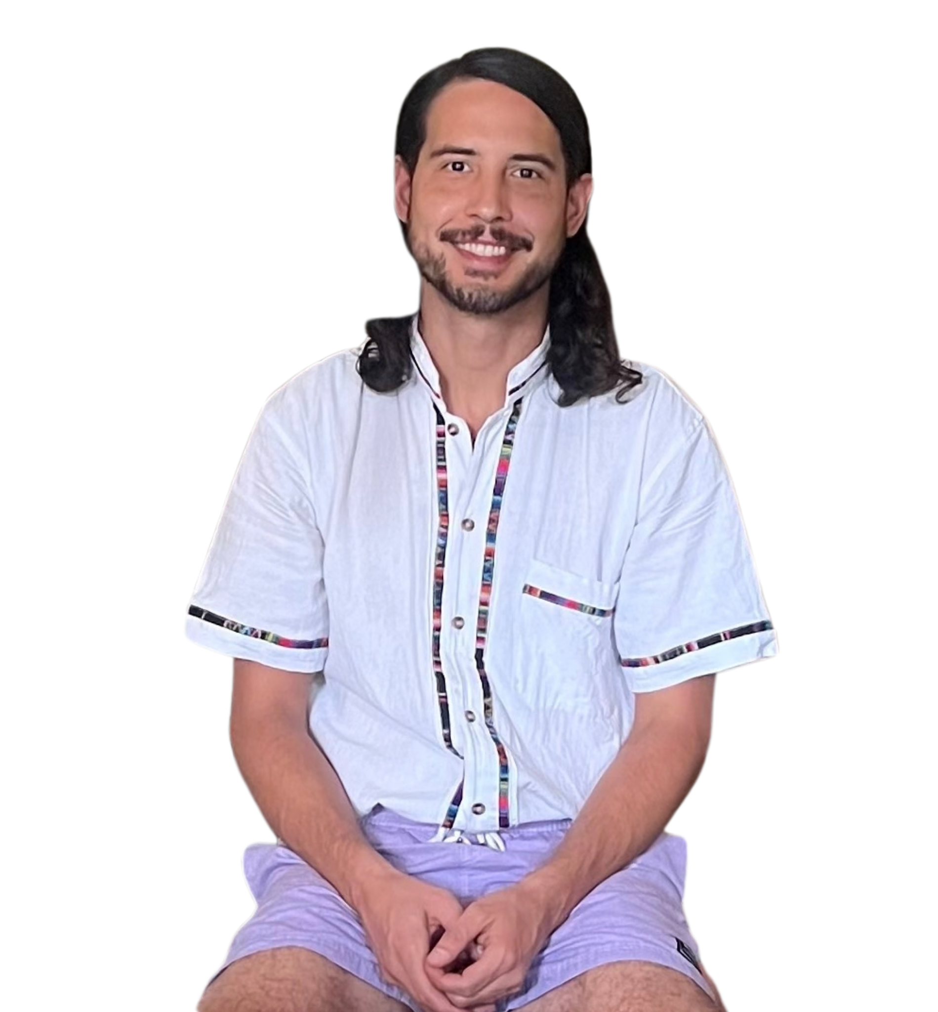 A smiling man with dark hair, beard, and mustache, wearing a white shirt with colorful accents and purple shorts, sitting with hands clasped, against a black background.