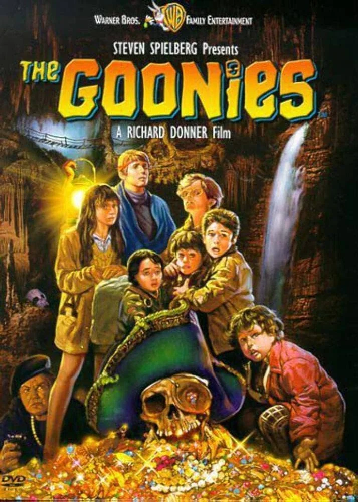 Movie poster for 'The Goonies' featuring seven children surrounding a skull and treasure, set in a cave with a waterfall in the background.