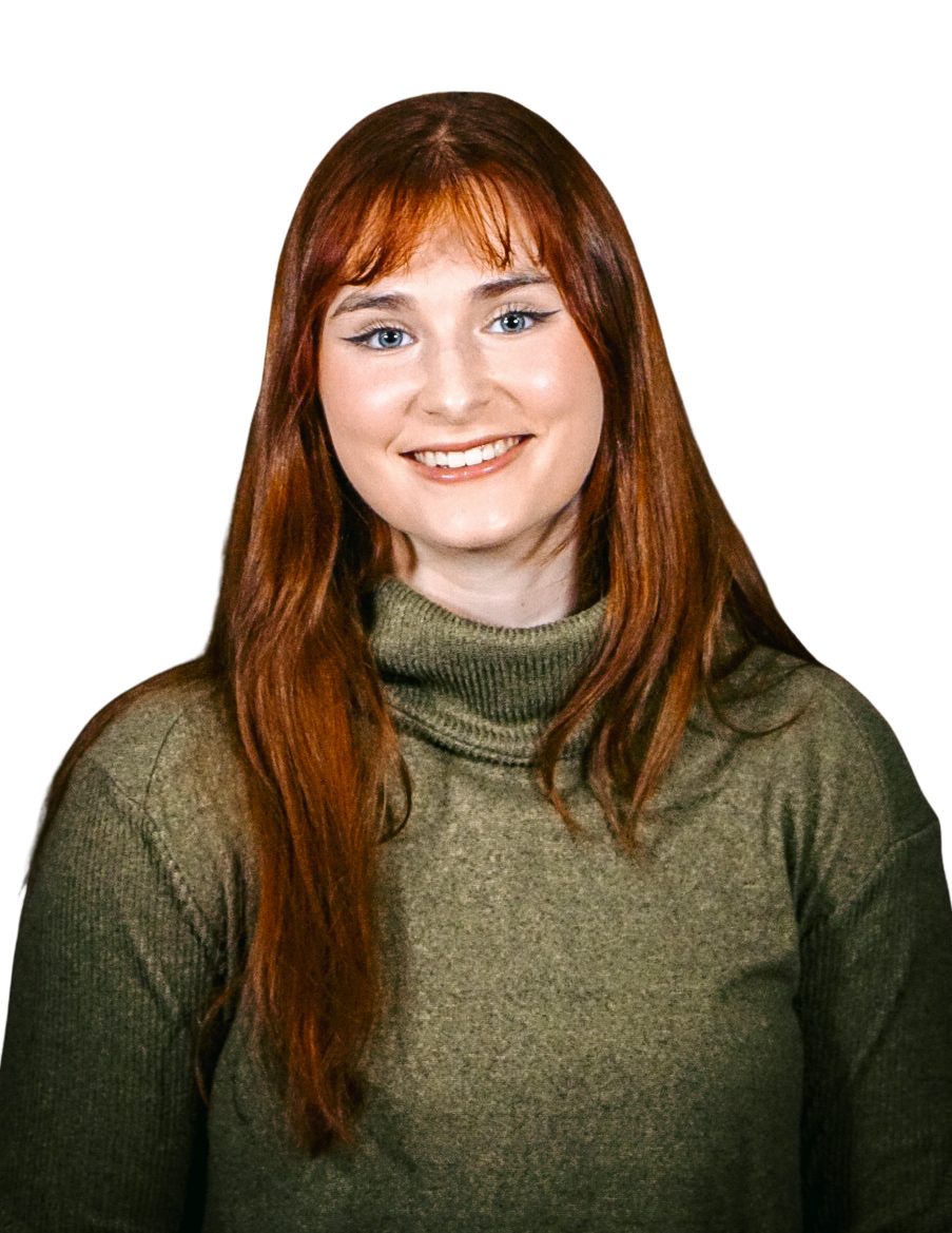 A woman with long red hair wearing a green turtleneck sweater, smiling against a colorful background.