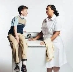 A boy sitting on an examination table talking to a nurse.