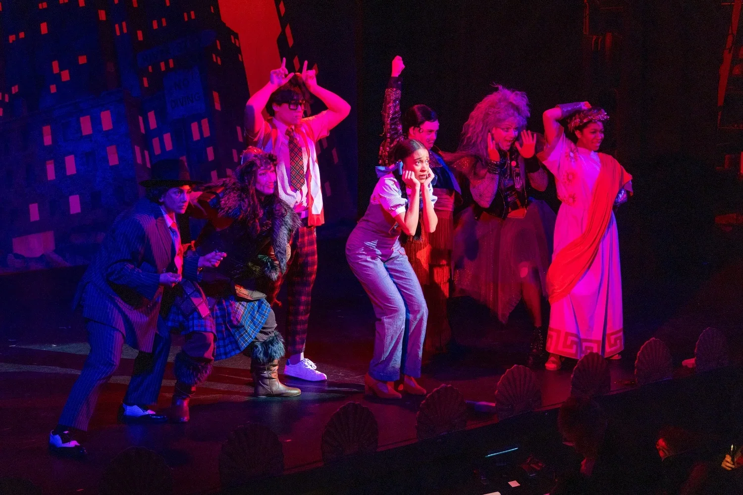The cast of a theatrical performance on stage, dressed in colorful costumes, making expressive gestures and poses under dramatic lighting.