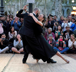 A couple is dancing passionately on a wooden floor outdoors, surrounded by a crowd of spectators watching and taking photos.