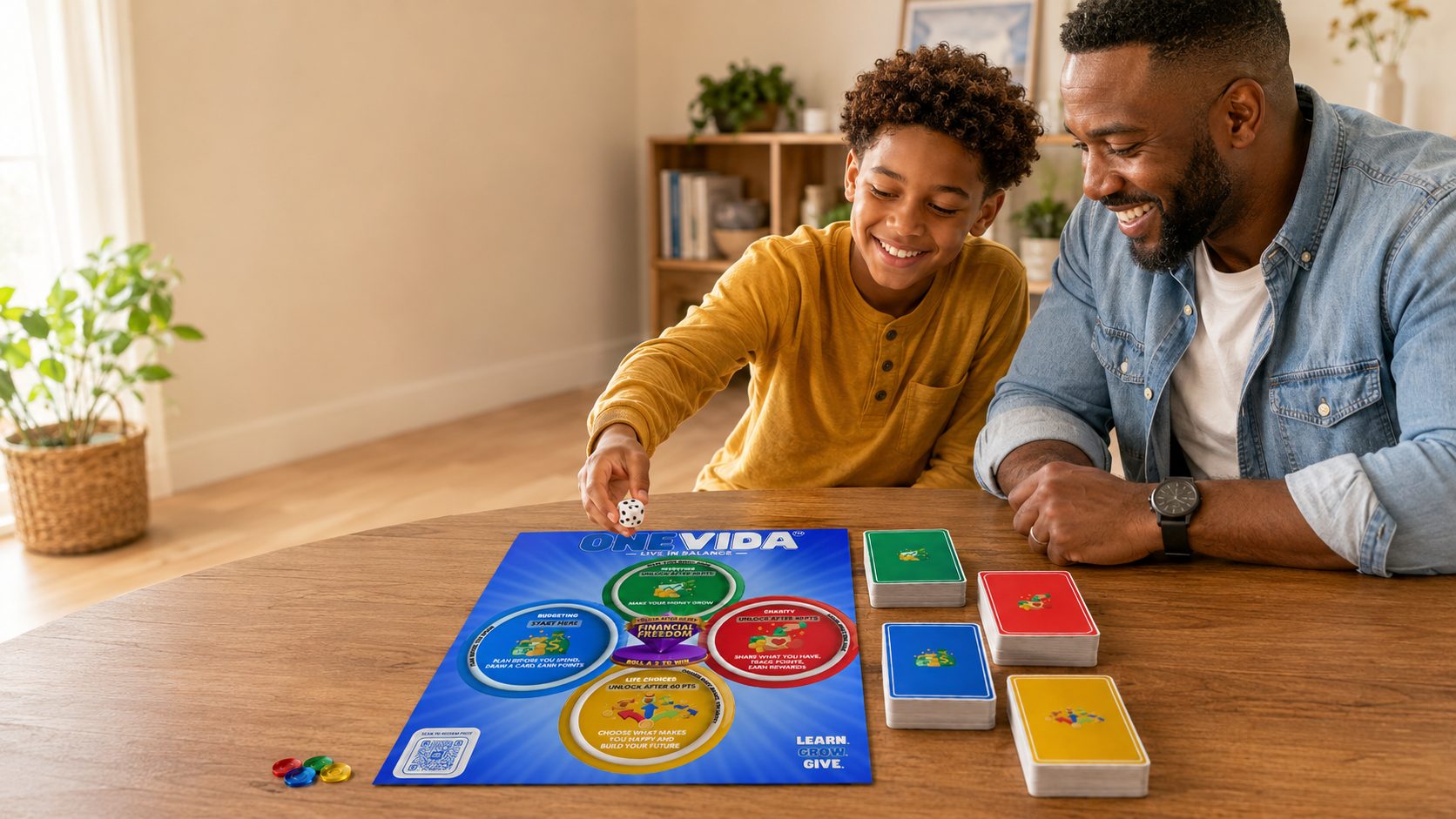 A young boy and a man playing a board game called OneVida at a wooden table. The boy is holding a die, and the game board and cards are visible. The background shows a room with a potted plant and a bookshelf.