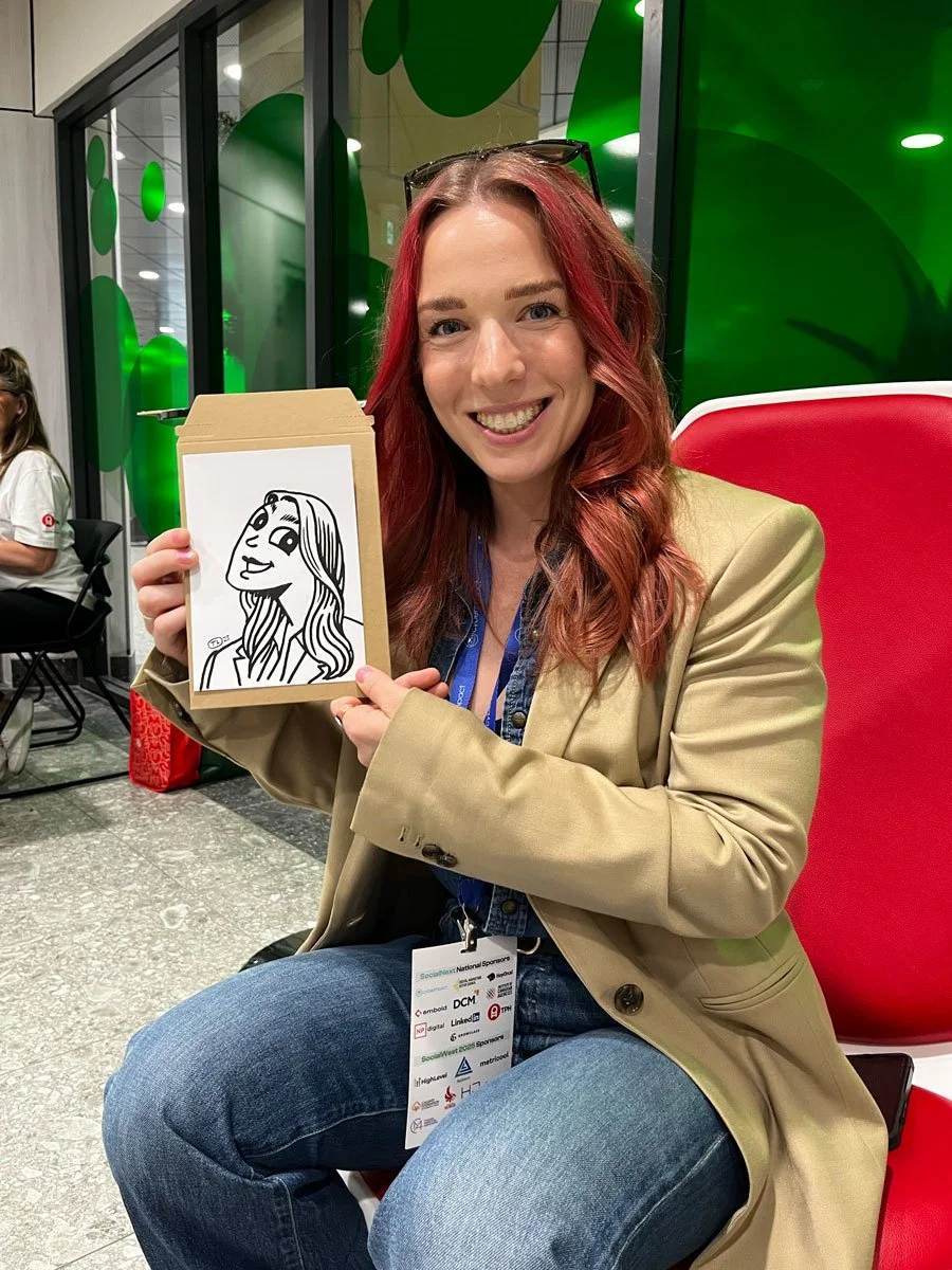 Woman in beige blazer and red hair, holding up a derpy portrait beside her face. The drawig capturing her hair nicely