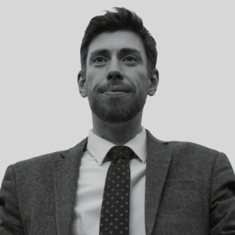 Black and white photo of a man in a suit and tie, looking slightly upward with a confident expression.