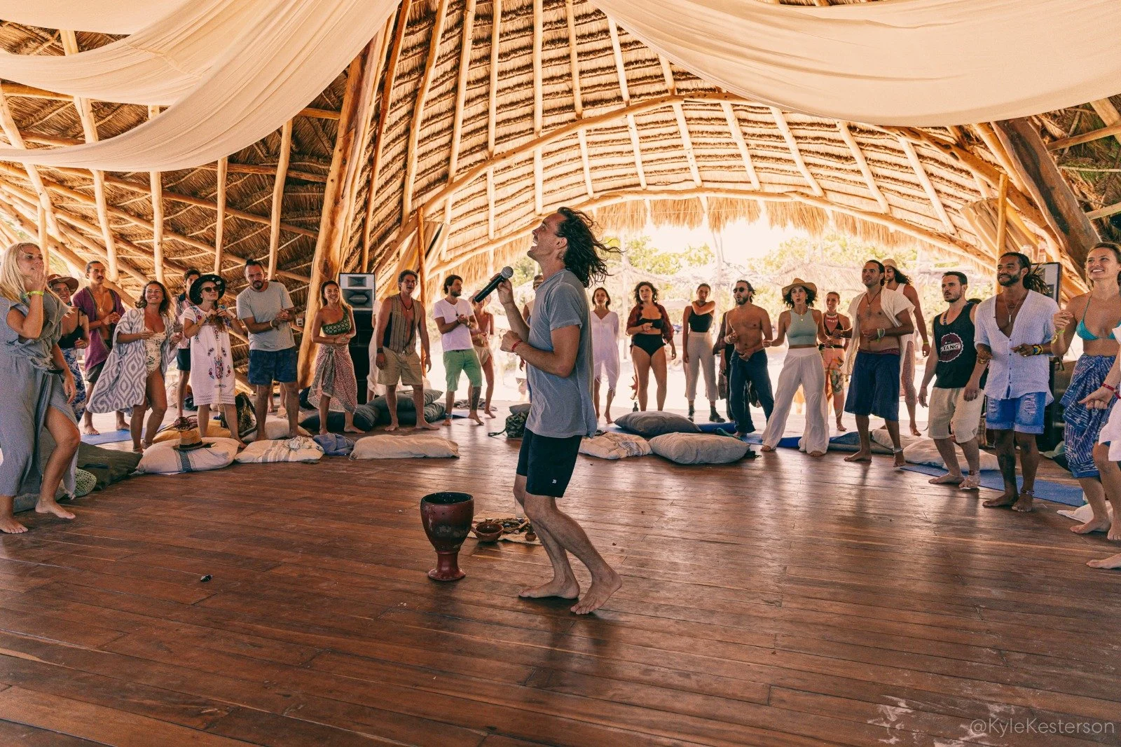 Un grupo de personas sentadas en círculo, participando en una sesión o reunión en un ambiente acogedor con techo de madera y una tienda tipi en el fondo.