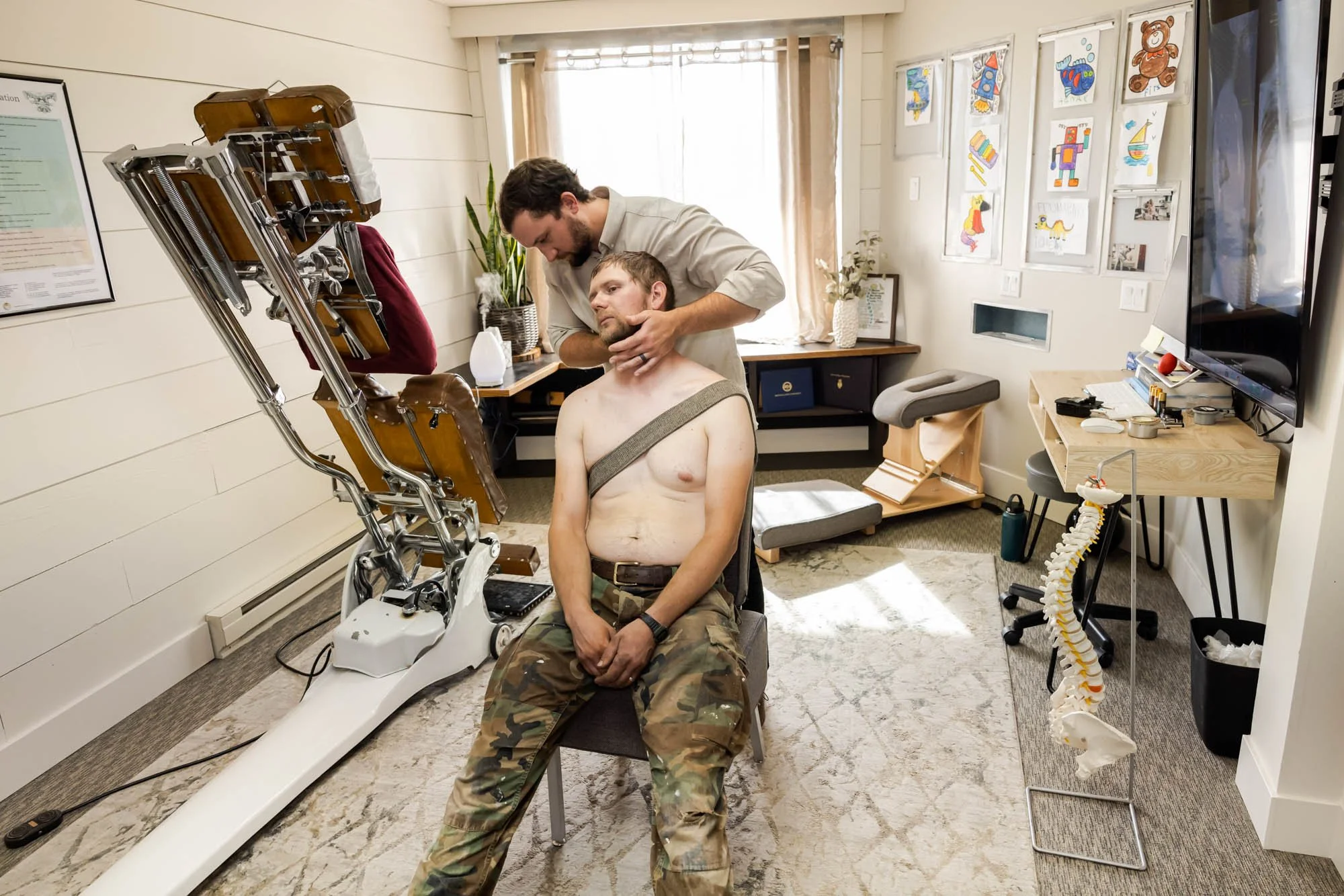 Dr. Peter Fennelly, a whitefish chiropractor, examining a man who has a neck injury, in a therapy room with children’s artwork on the wall.